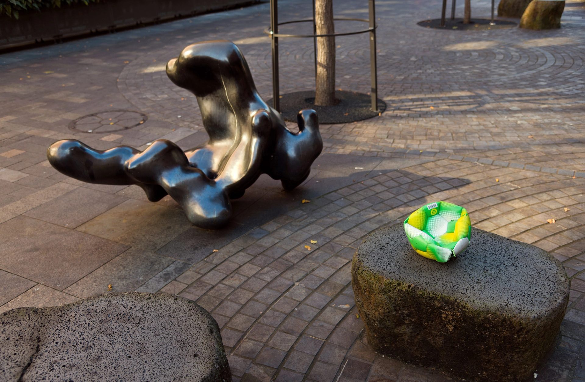 A black sculpture and a yellow and green soccor ball sit on the footpath.