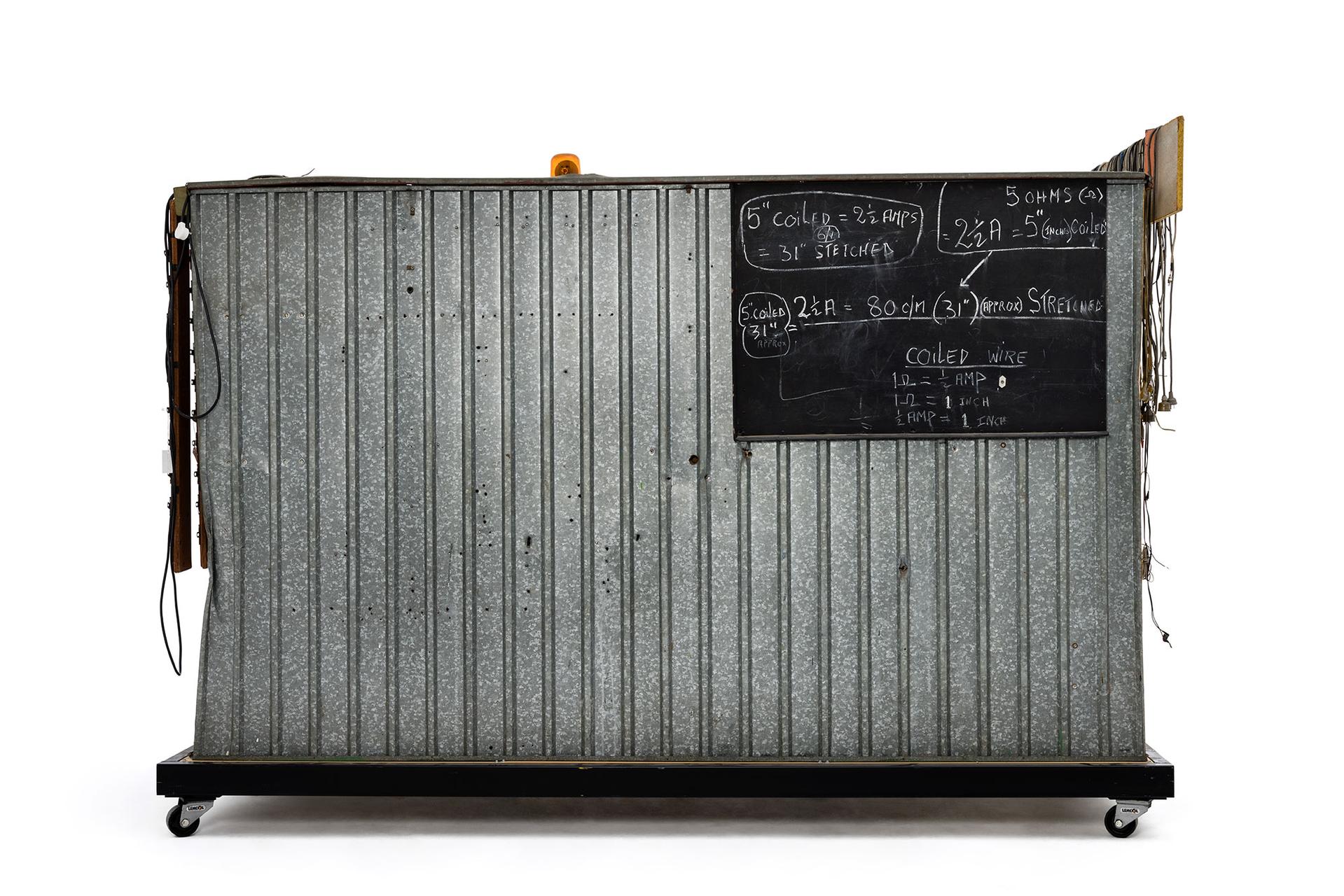 Green and yellow metal 'garden' shed containing elaborate electronic systems built into the interior. Inside the shed is a compartment which contains a seat where the user can sit and be suffused with radio waves produced by the electronic system.