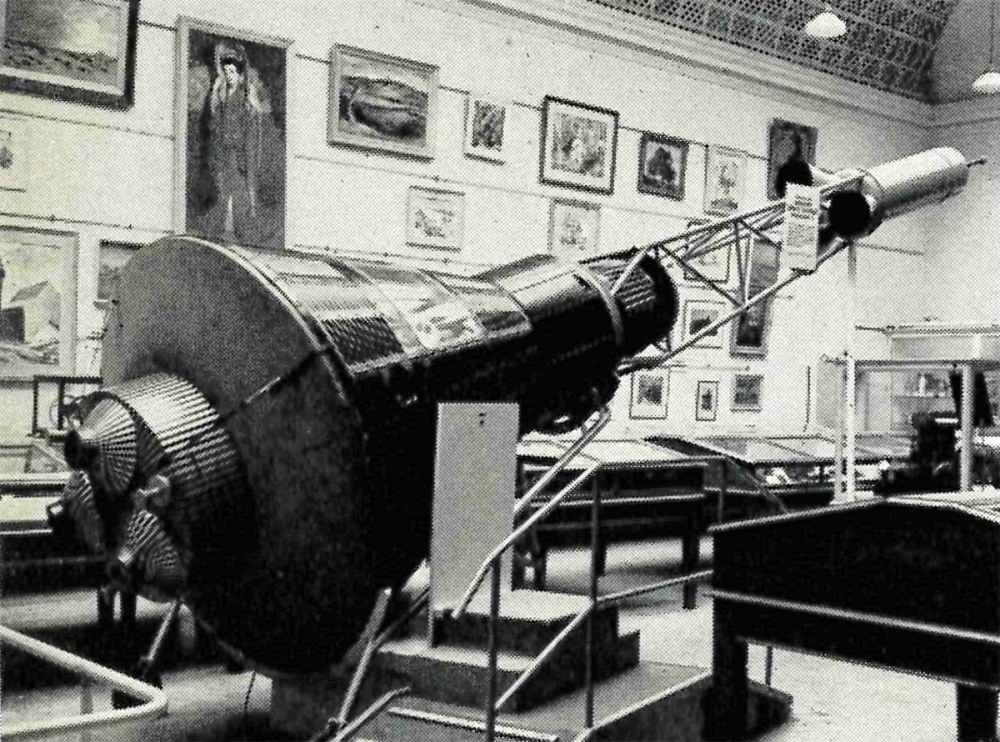 Black and white image of the Mercury Space Capsule at the Broken Hill branch museum with pictures hanging in the background