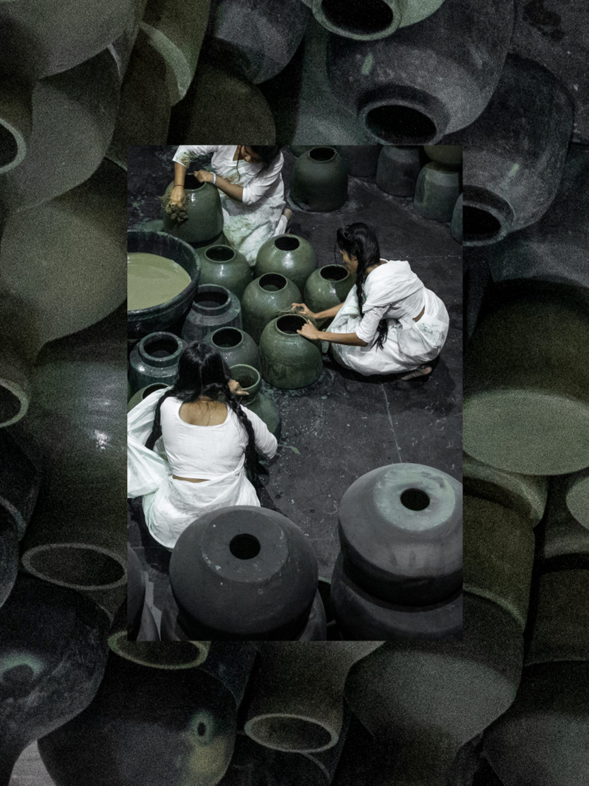 Five people dressed in white sit on the floor around black pots and surrounded by black pots.