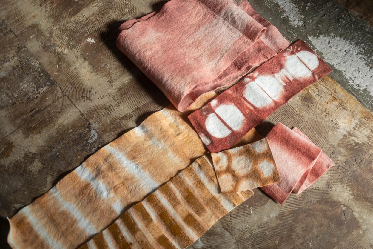 Four textiles of varying sizes, colours and patterns are laid out atop a dark brown fabric.