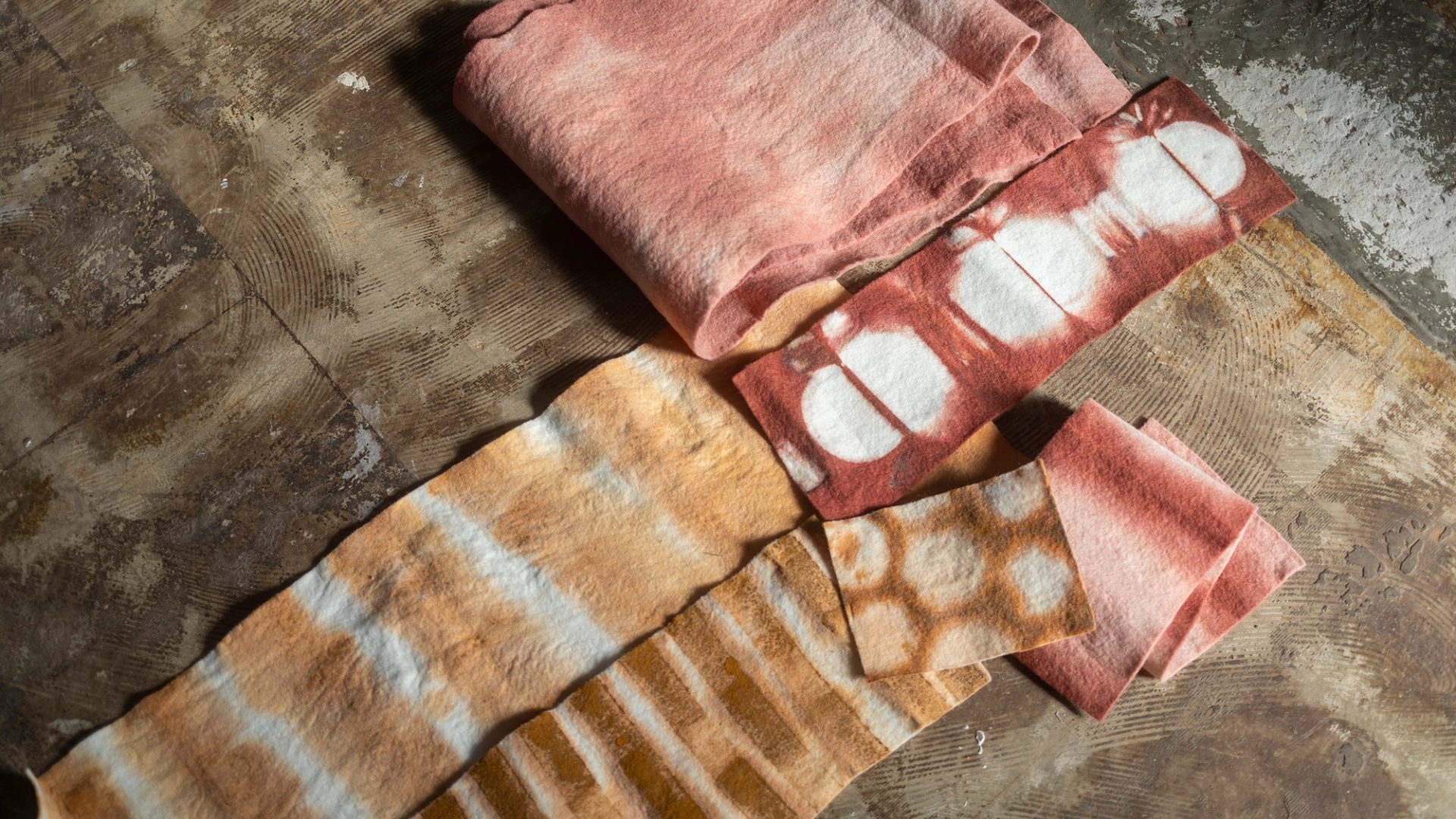 Four textiles of varying sizes, colours and patterns are laid out atop a dark brown fabric.