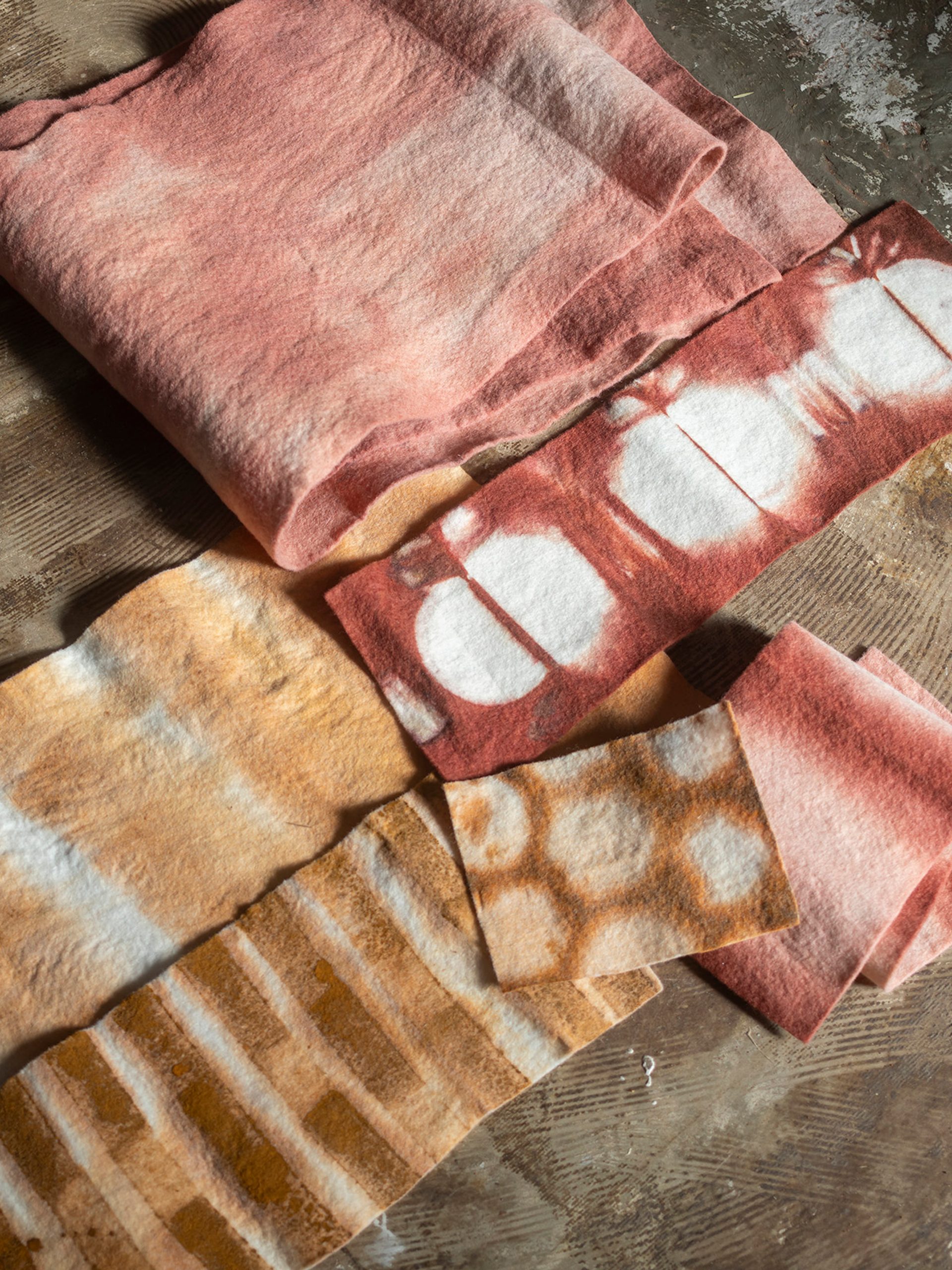 Four textiles of varying sizes, colours and patterns are laid out atop a dark brown fabric.