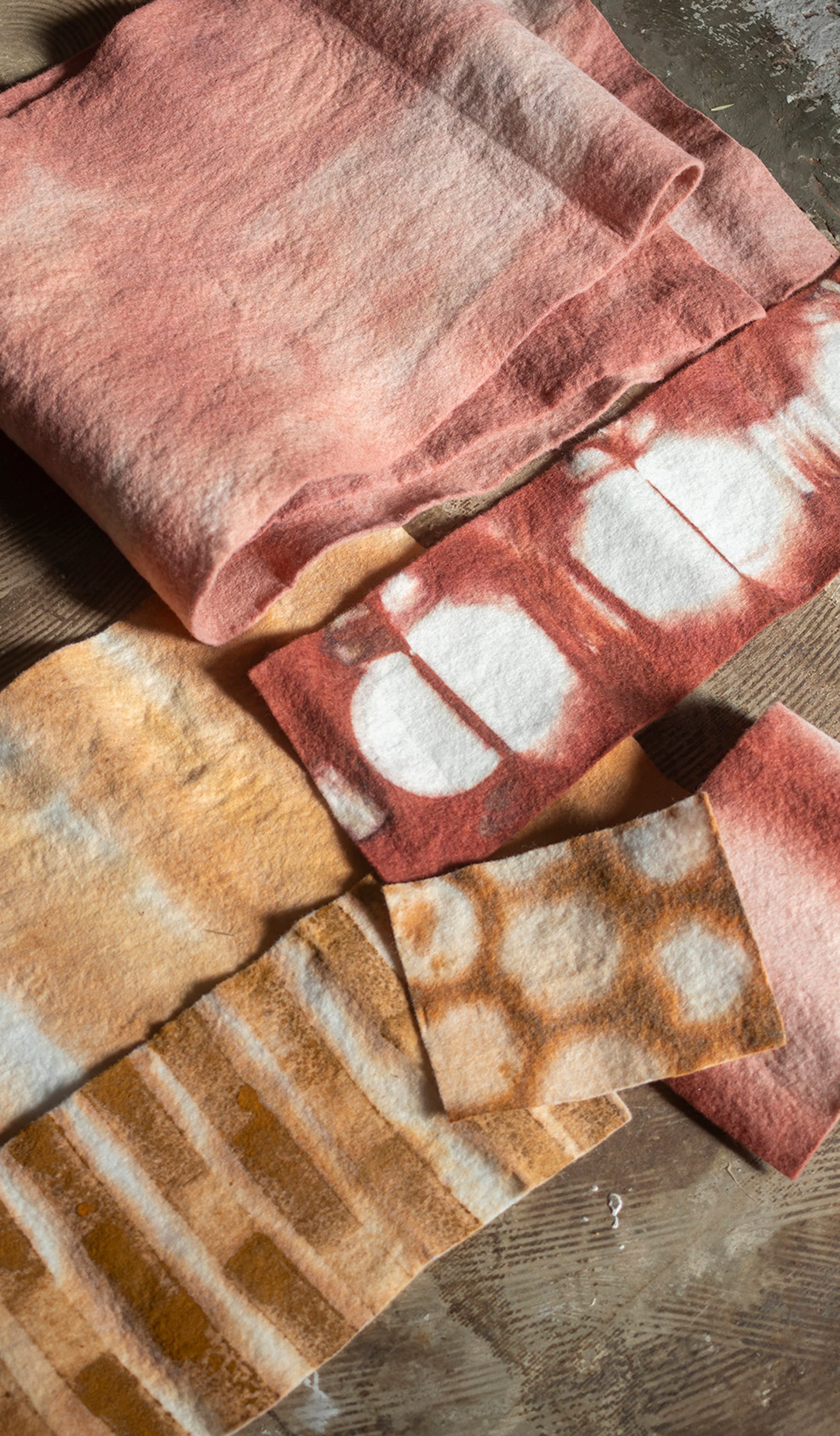 Four textiles of varying sizes, colours and patterns are laid out atop a dark brown fabric.
