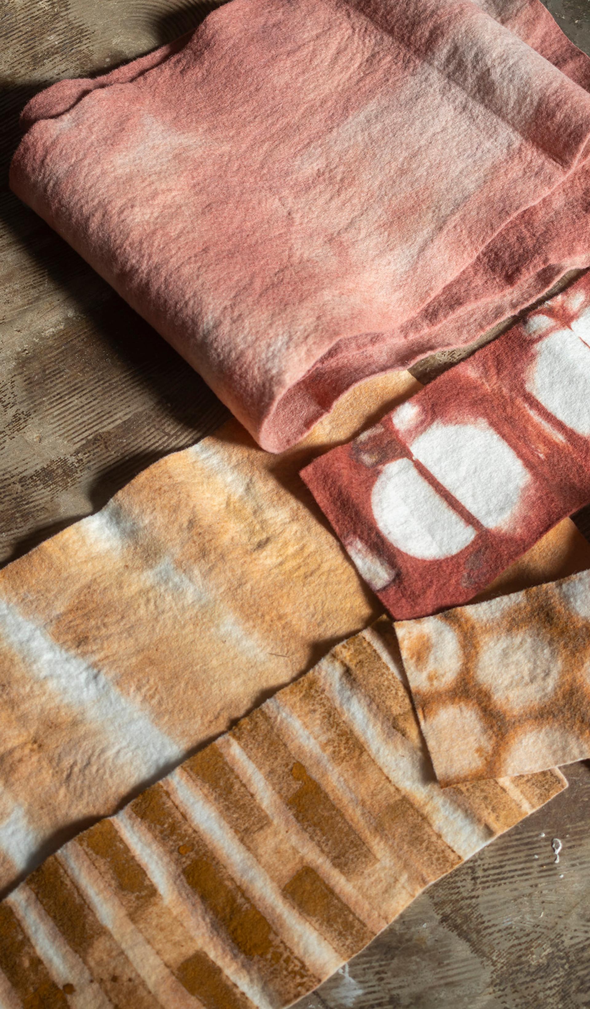 Four textiles of varying sizes, colours and patterns are laid out atop a dark brown fabric.