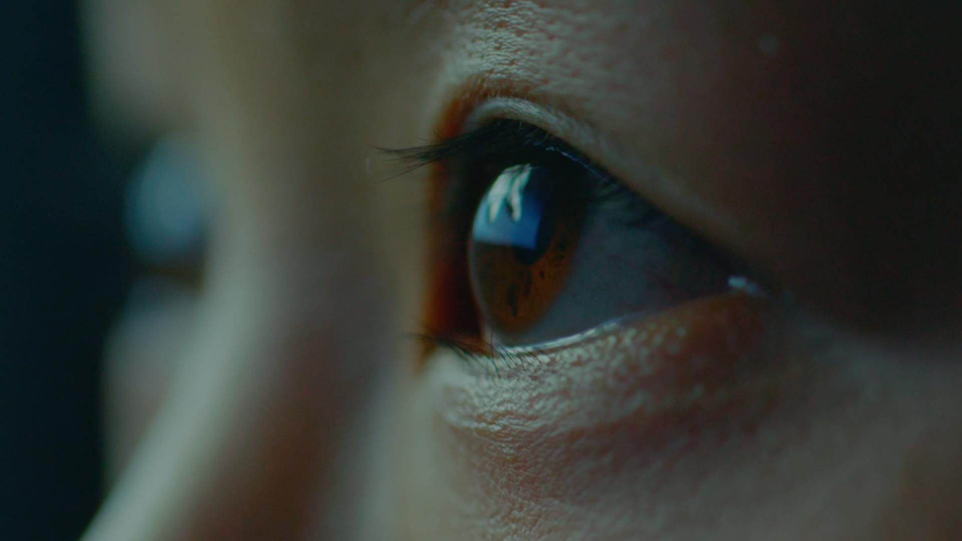 Close up of eyes looking upwards with the corner of a screen reflected in the eye