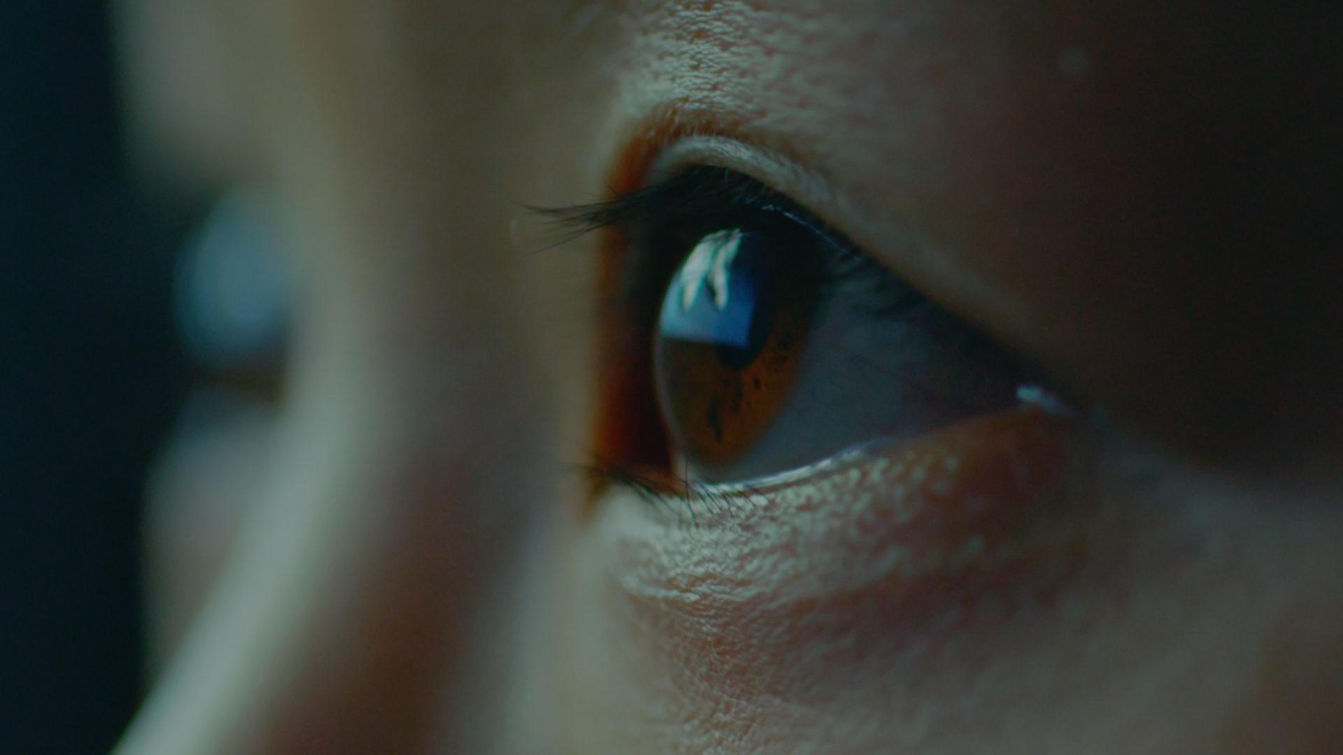 Close up of eyes looking upwards with the corner of a screen reflected in the eye