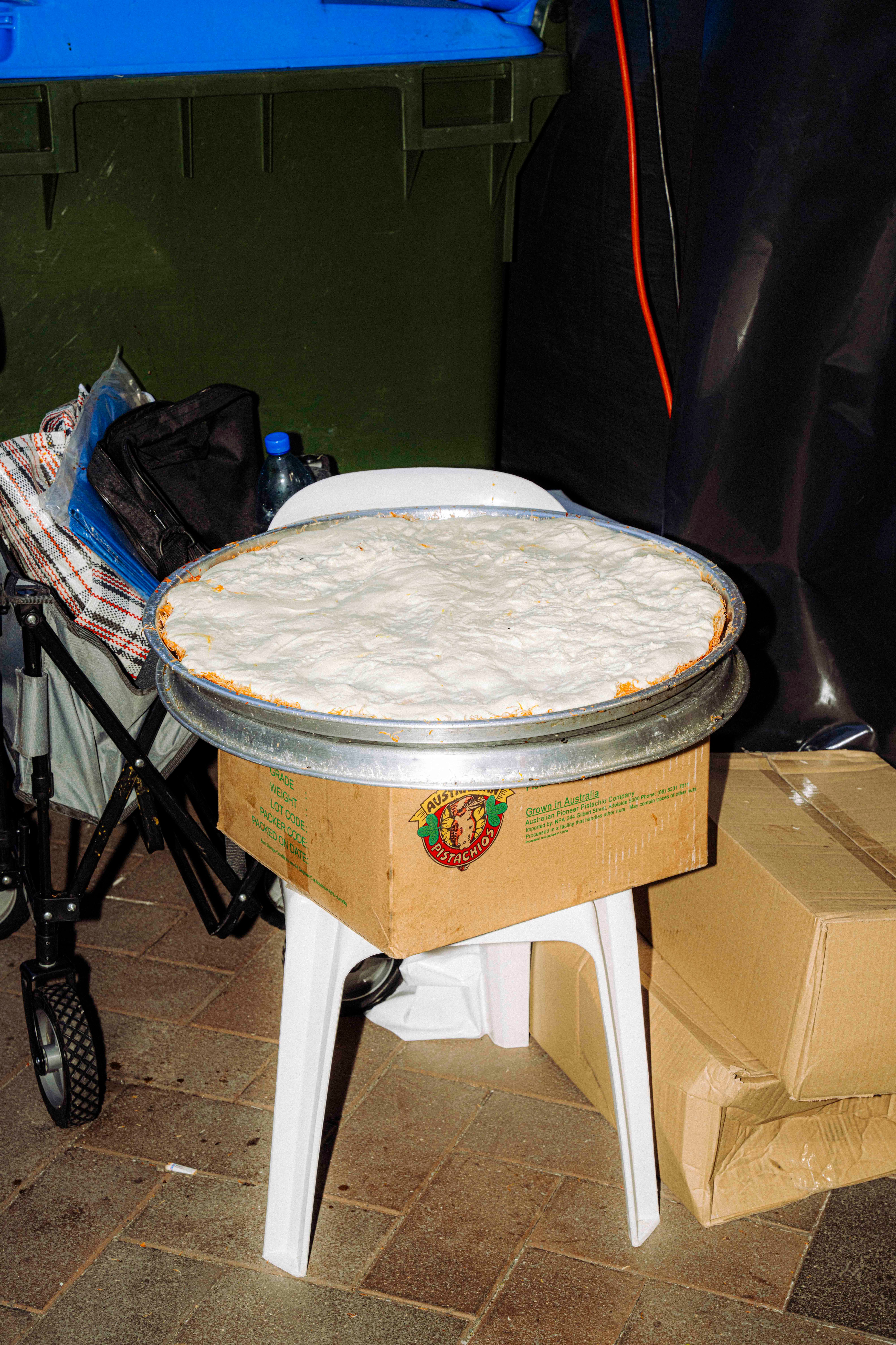 A cardboard box labelled ‘Australian Pistachio’ sits on a white plastic chair, underneath a large round metal tray filled with a smooth pale substance.
