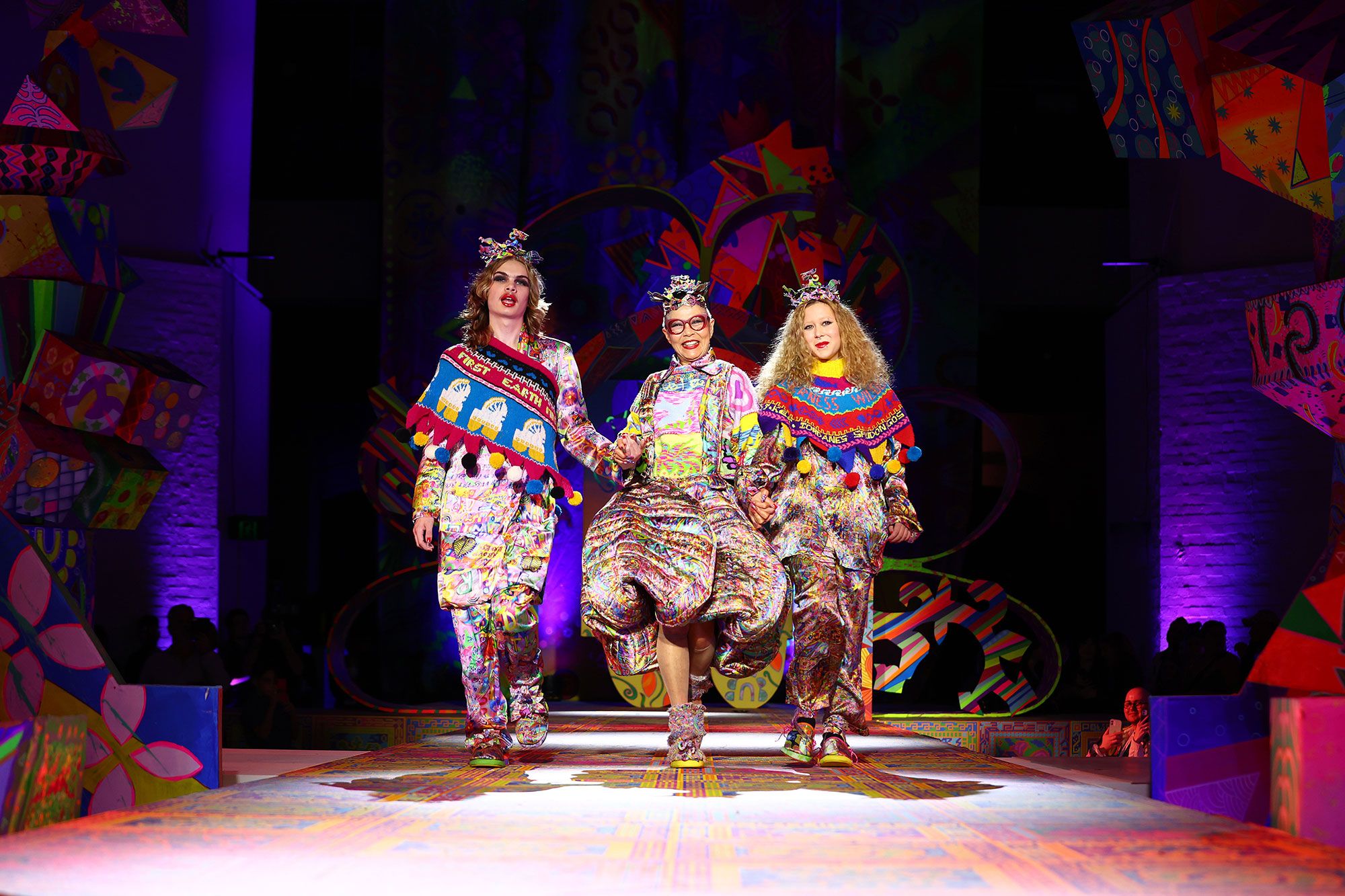 Three models walk on the runway holding hands