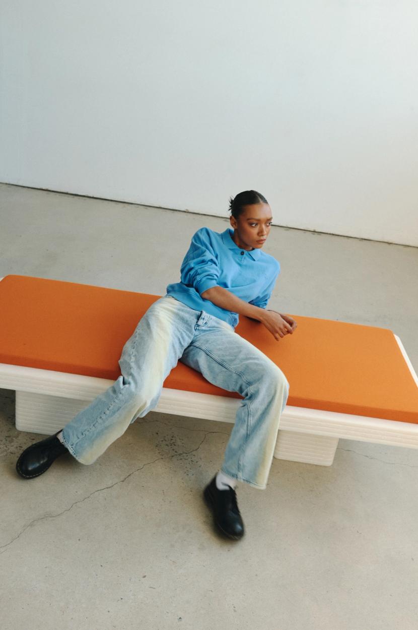 Orange cushion above a dynamic white daybed with figure wearing blue sitting atop