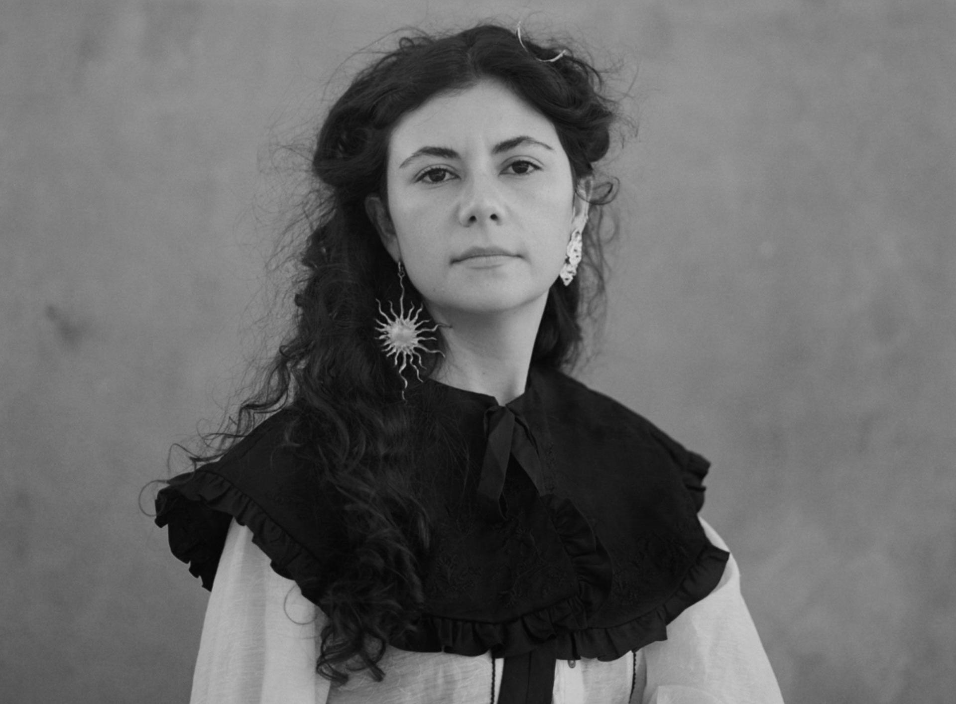 Indira Elias looking at the camera, wearing a Sun-like earring.
