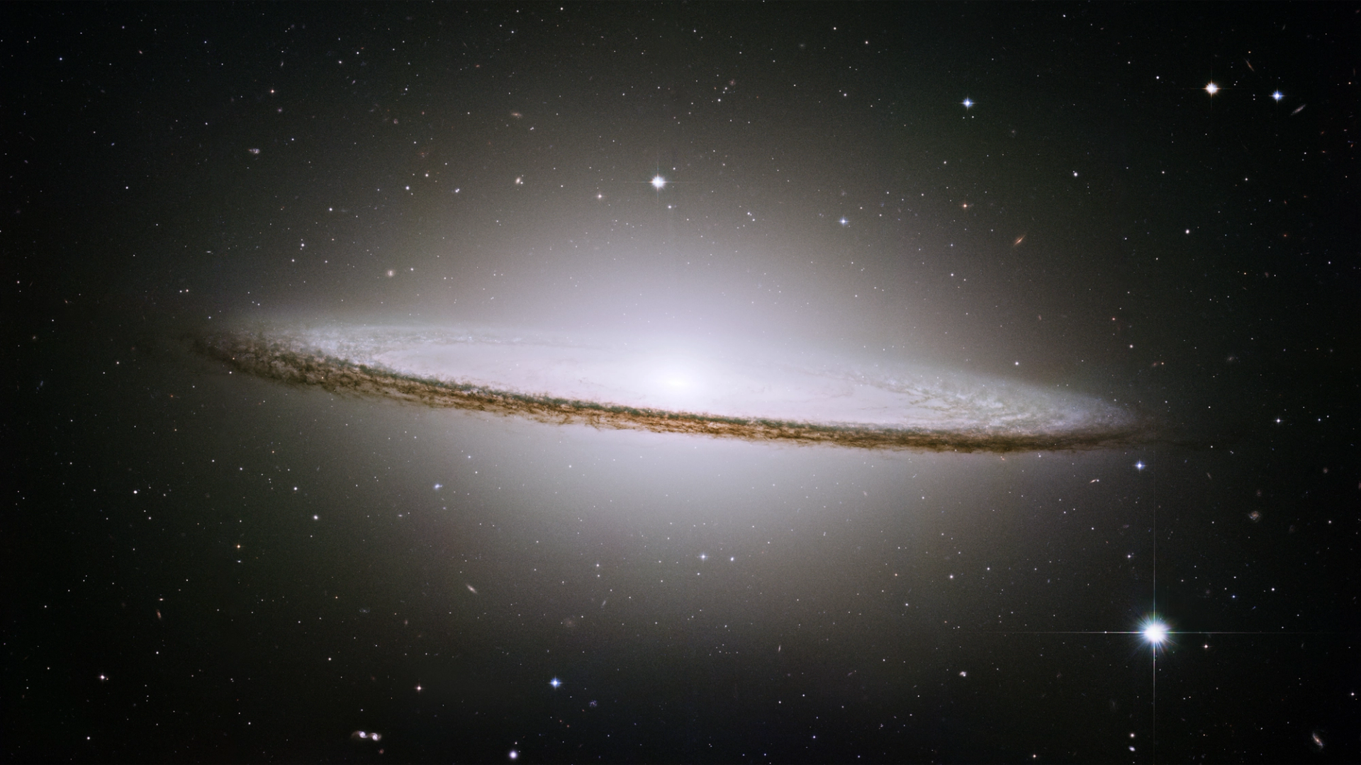 A telescopic image of the Sombrero Galaxy, showing a brilliant white, bulbous core surrounded by a ring of thick dust lanes.
