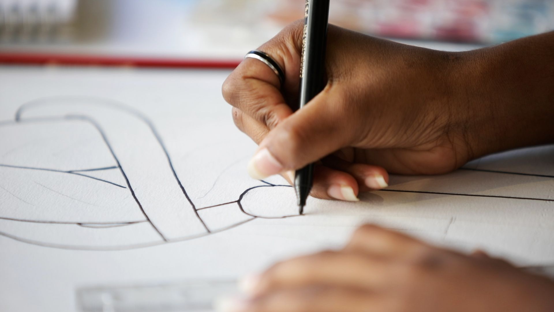 A hand holding a pen draws a curved black line on a piece of paper