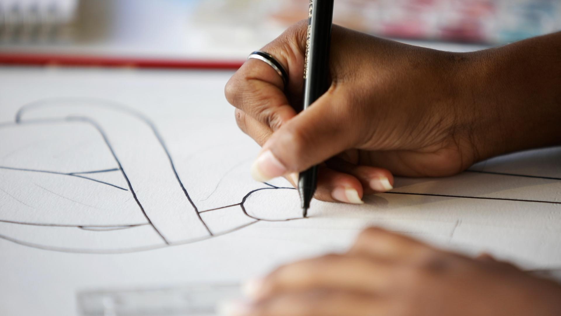 A hand holding a pen draws a curved black line on a piece of paper