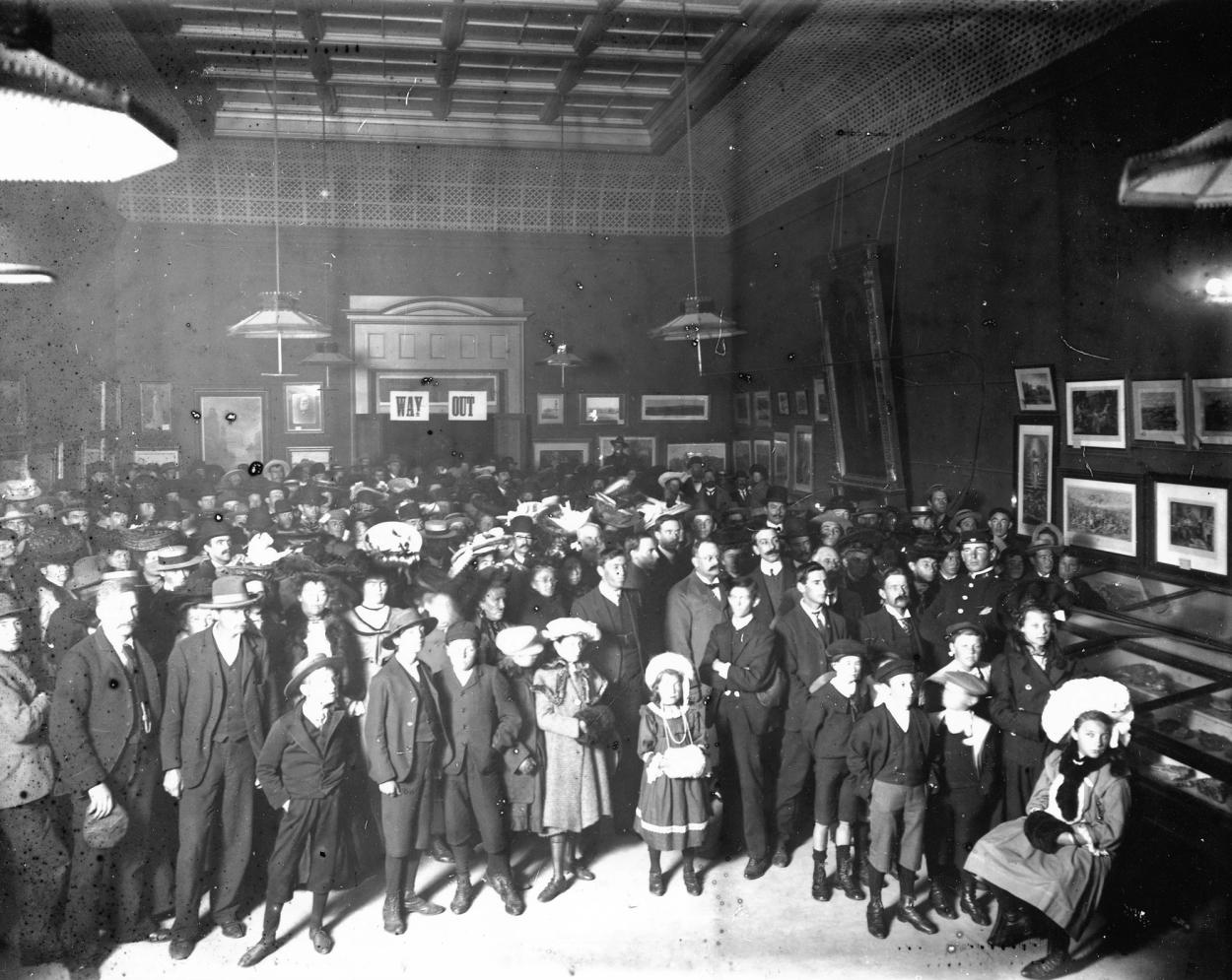 Black and white photograph of a large group of people standing in a museum gallery