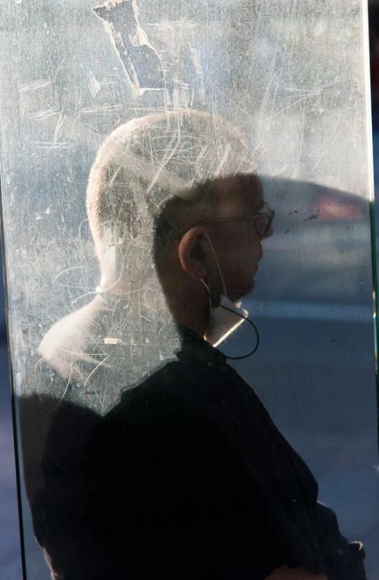 A figure sitting at the bus stop, the photograph is taken through the perspex of the bus stop shelter.