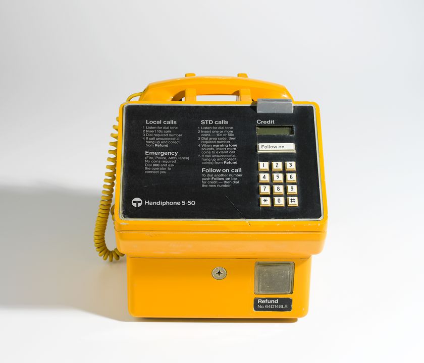 Yellow public telephone, with instructions, twelve push buttons for the dial, and a coin slot.
