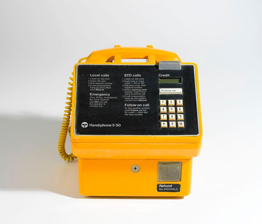 Yellow public telephone, with instructions, twelve push buttons for the dial, and a coin slot.