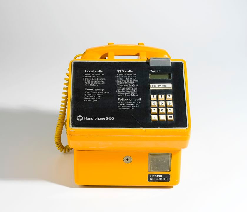Yellow public telephone, with instructions, twelve push buttons for the dial, and a coin slot.