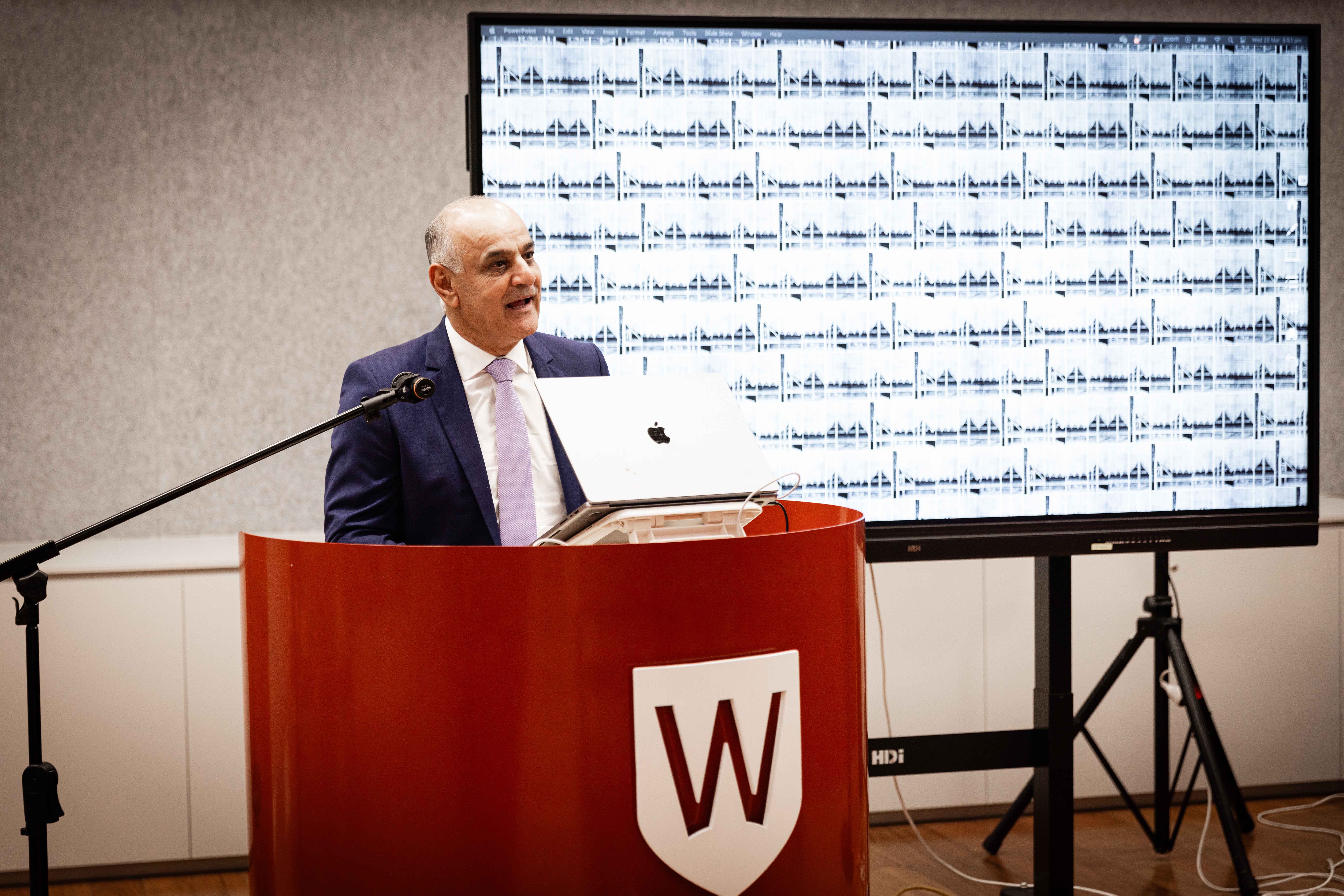Person in a suit addressing people from behind a podium.