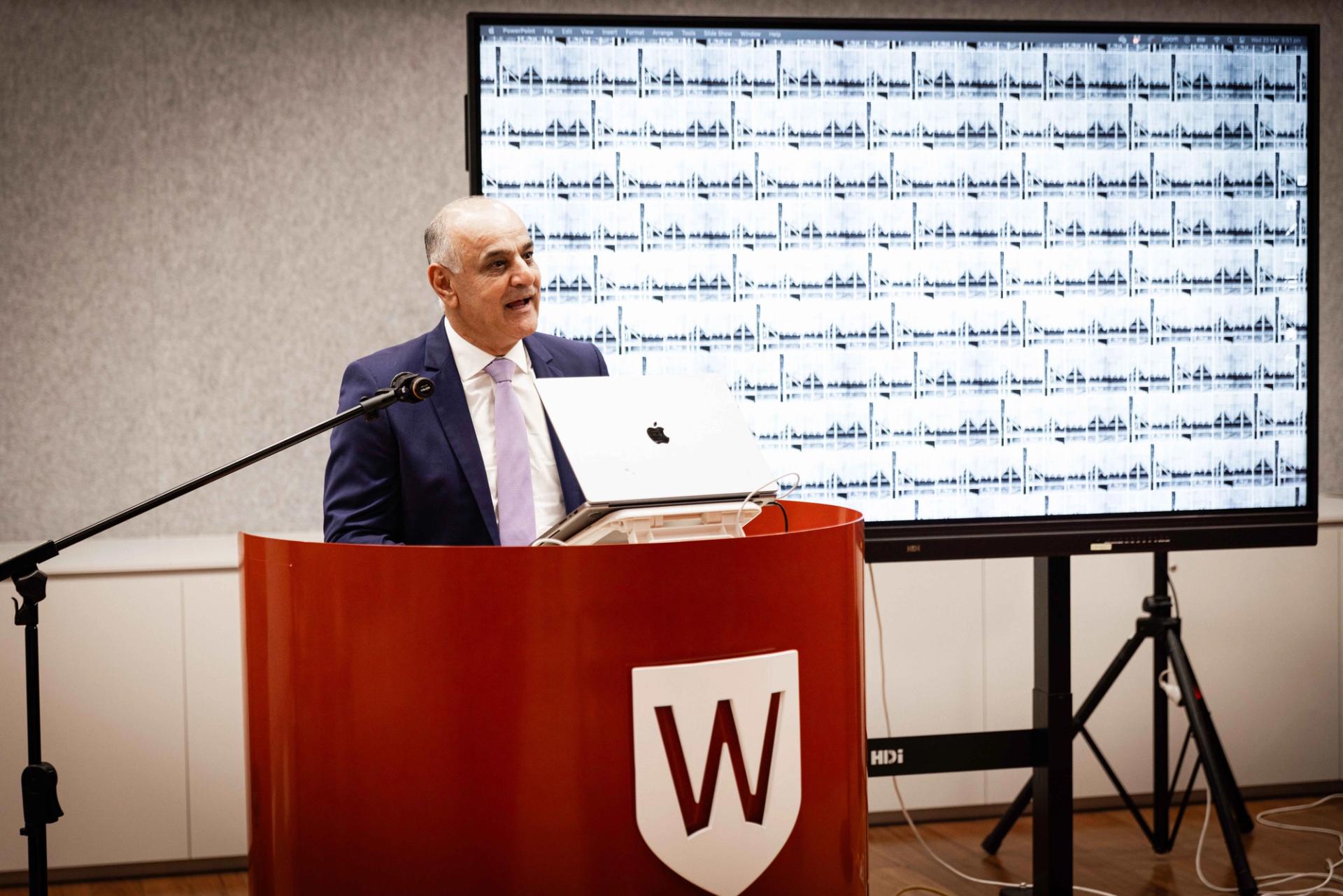 Person in a suit addressing people from behind a podium.