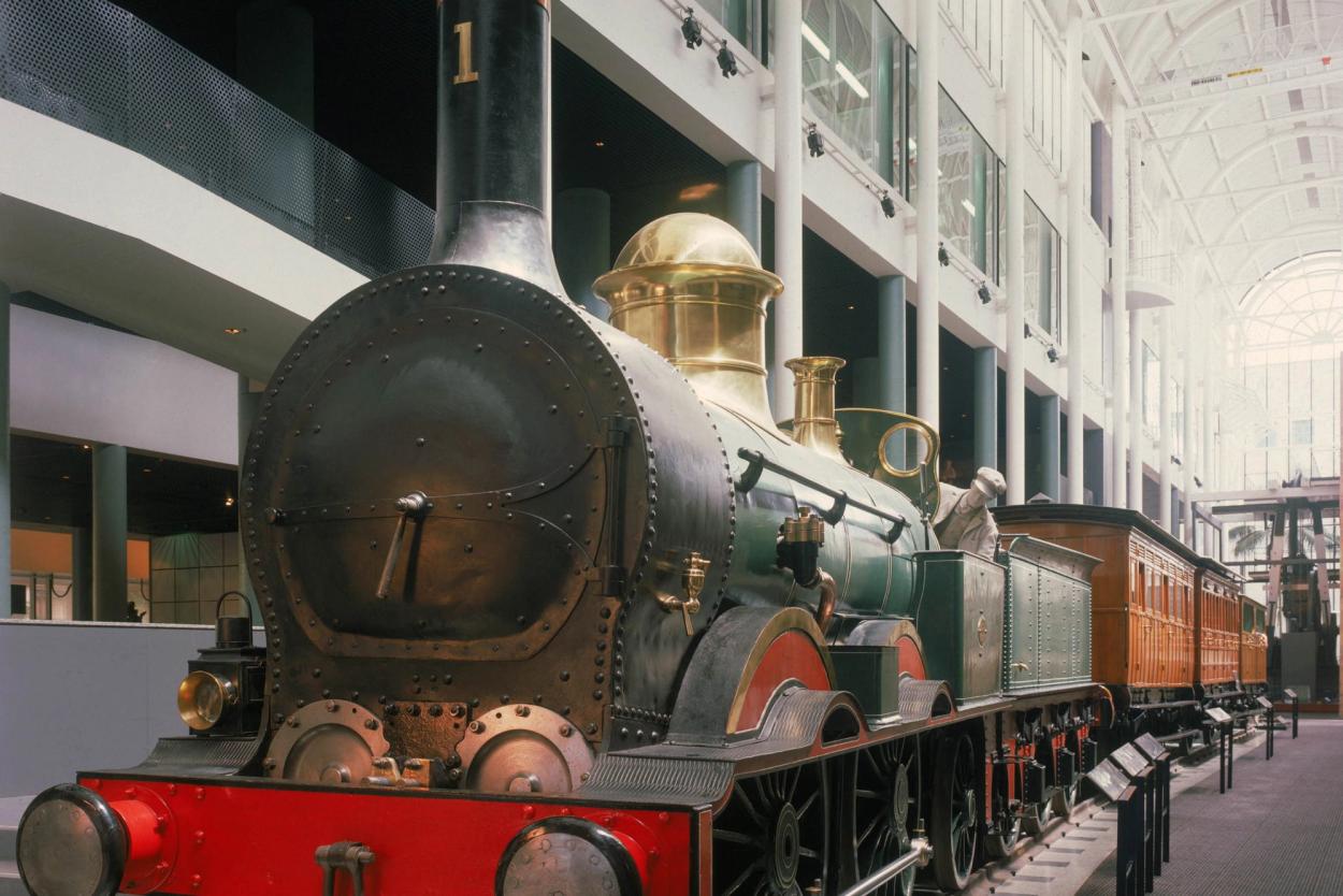 A large dark green locomotive with gold and black viaducts. The wheel caps and front of the locomotive are painted red.