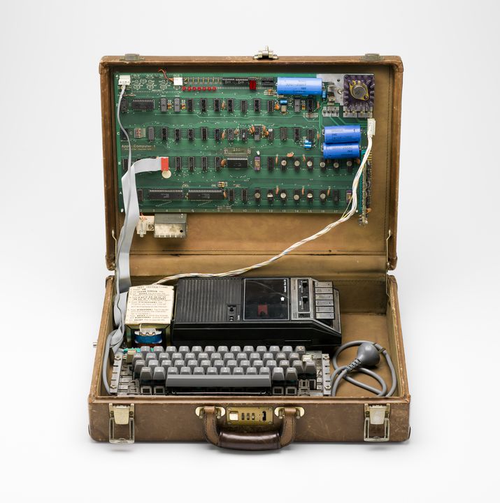 briefcase with a keyboard and visible motherboard connected by wires, with the electrical plug sitting sinise it.