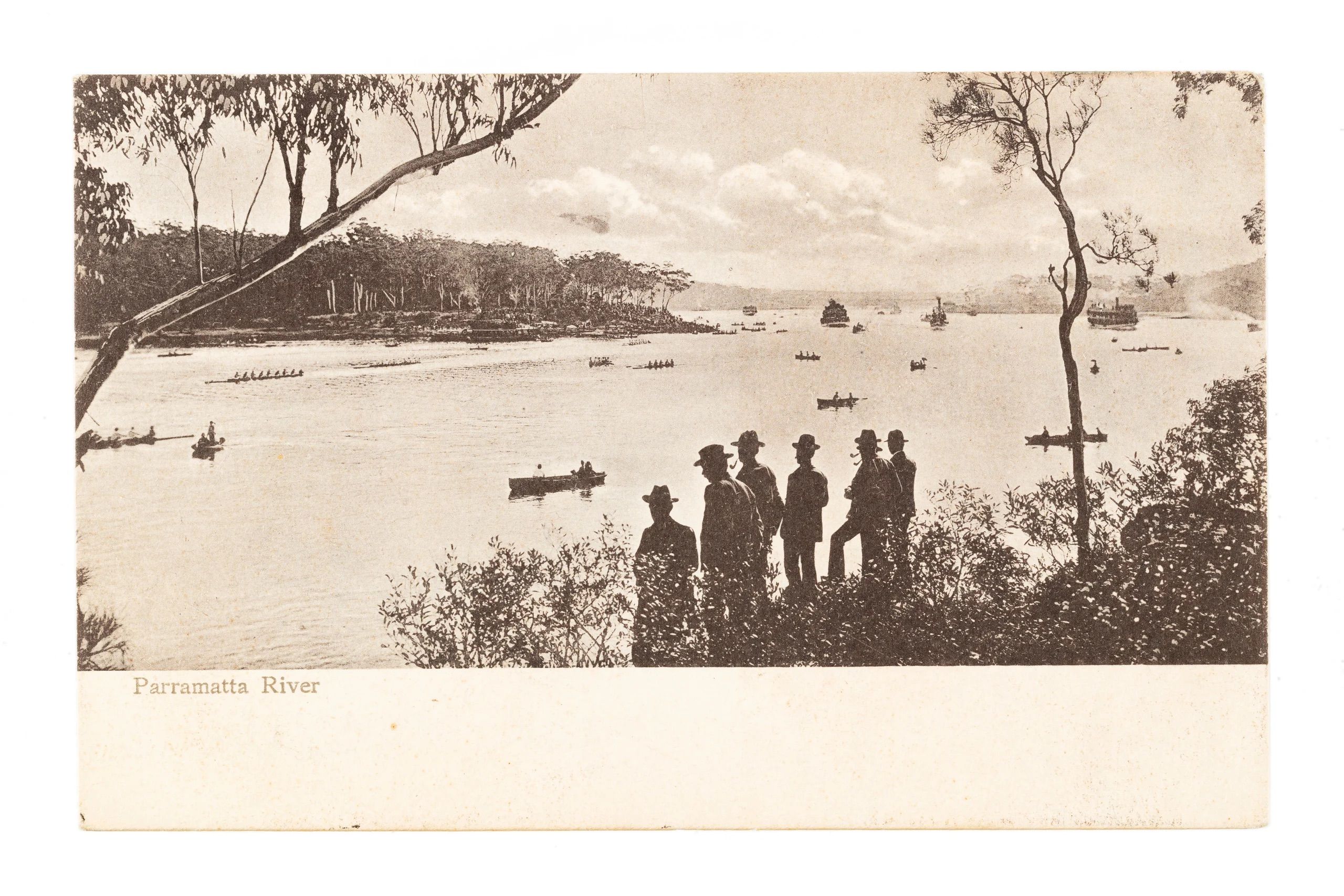 A river with its banks covered in shrubs and trees. There are boats on the water and six male figures in hats standing on the bank. Text on the left reads 'Parramatta River'.