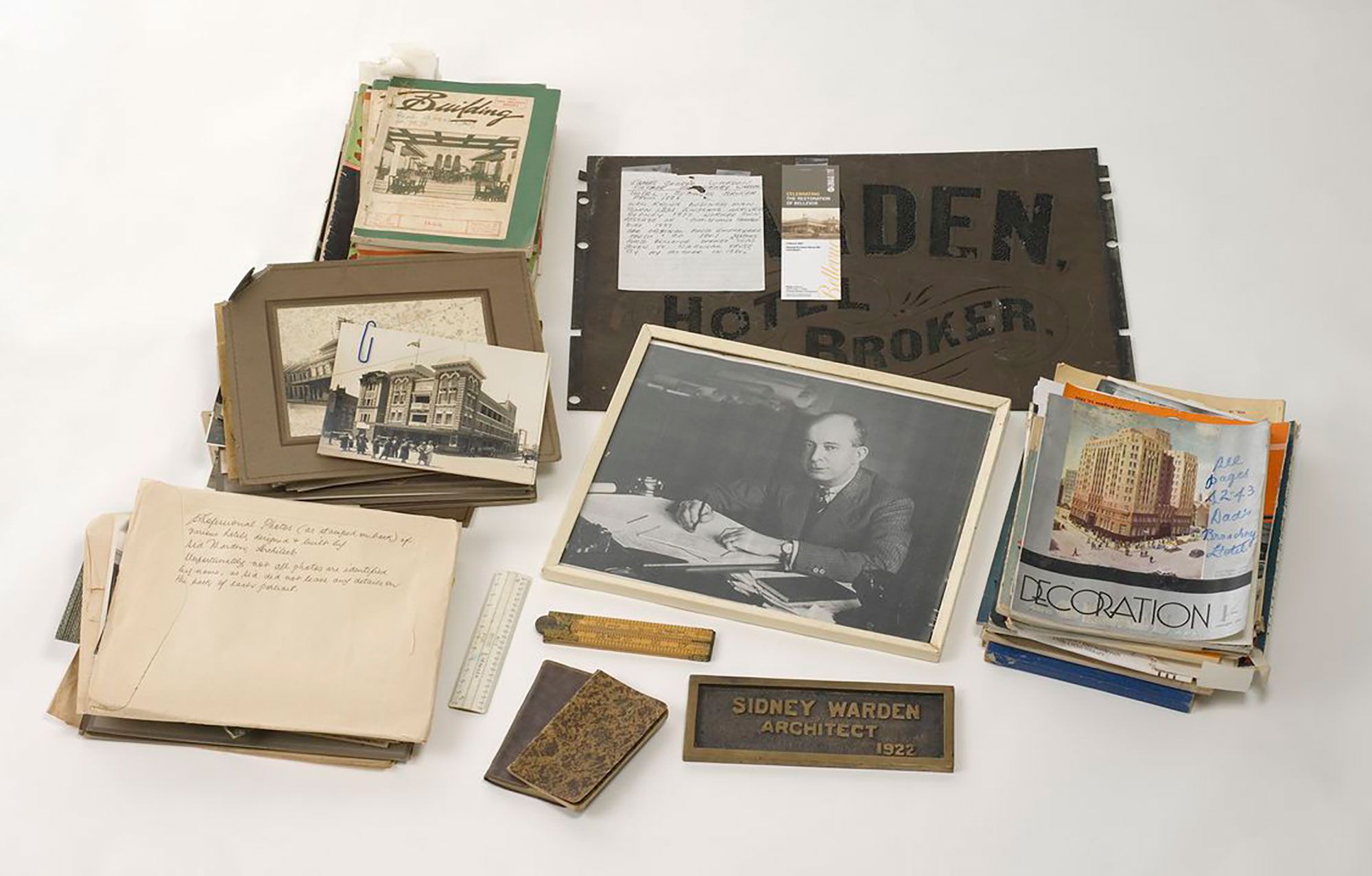 An archive documenting the architectural work of Sidney Warden and includes a small number of architect's renderings, including elevations of the Chinese National Society, the Oxford Hotel, the Mayfair Hotel, the Tennyson Hotel, Botany and an interior proposed for the City Tattersall's Club. The archive also includes several copies of architectural journals featuring photos and reviews of Warden's work. The journals are primarily 'Building' and 'Decoration and Glass'. There are two brass plates: 'Sidney Warden Architect 1922', and 'Warden Hotel Broker', which presumably dates from 1886, when Warden snr commenced business as a hotel broker. Other personal items include a framed reproduction portrait photo of Sidney Warden, two notebooks containing jottings on building jobs, two rulers, and a payments book for 1937.
