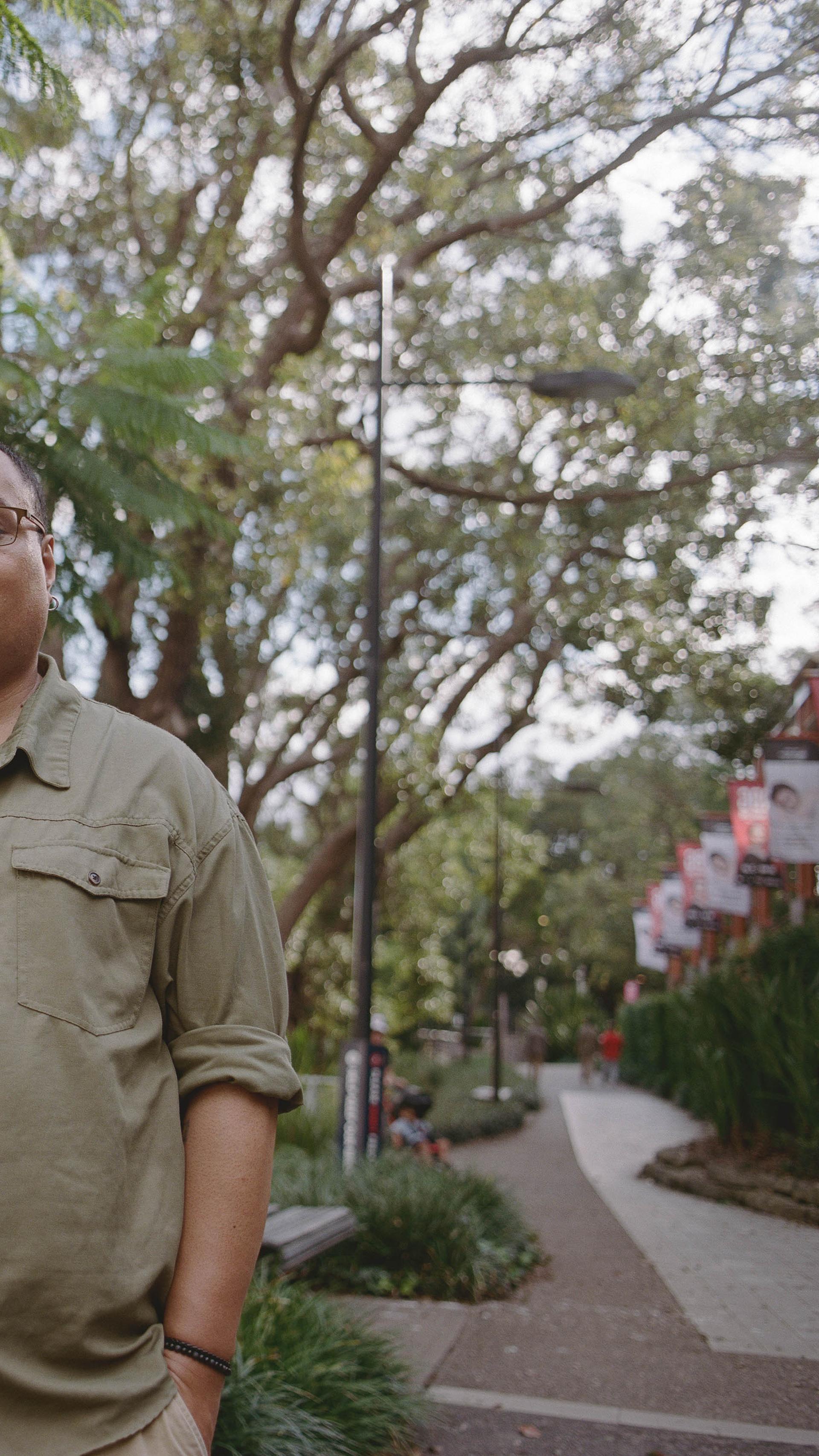 Person looks down at the camera, with hands in pockets, standing outside on a footpath.