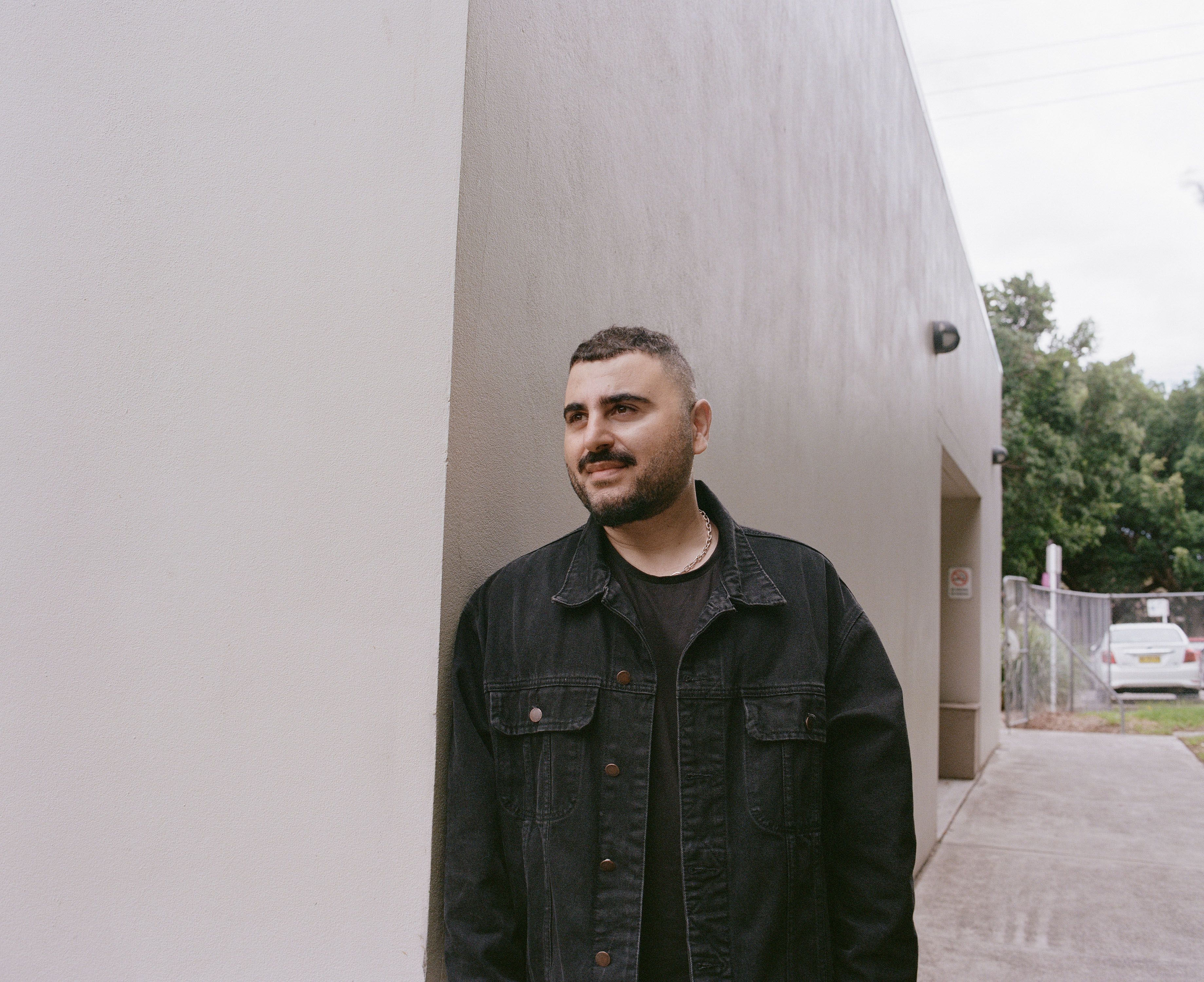 Person leans on the corner of a building, outside.