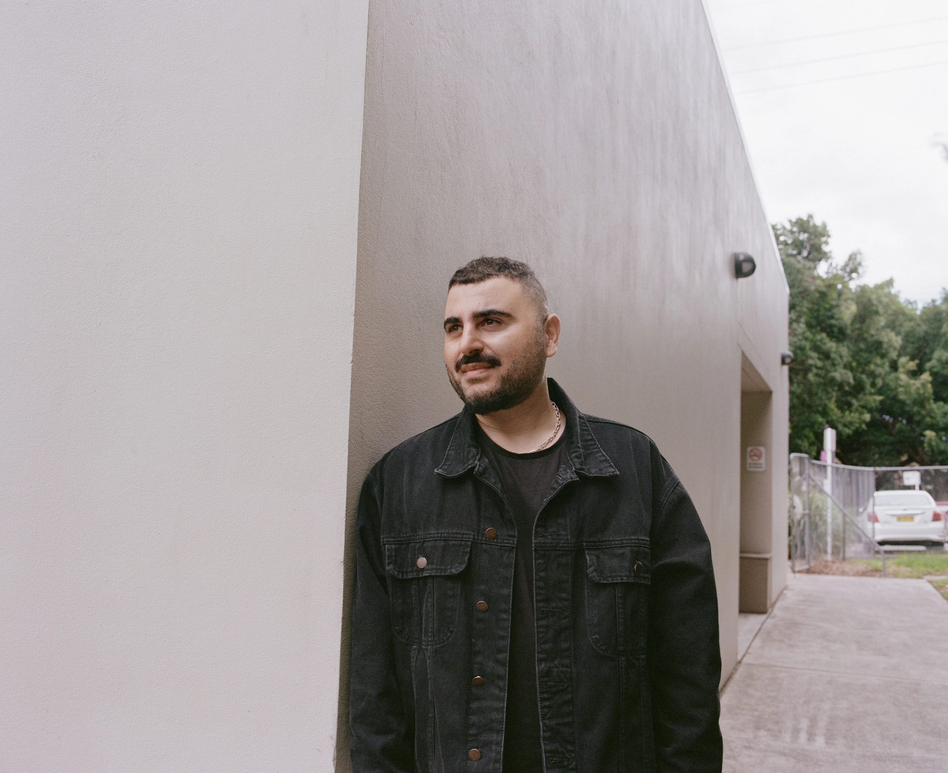 Person leans on the corner of a building, outside.