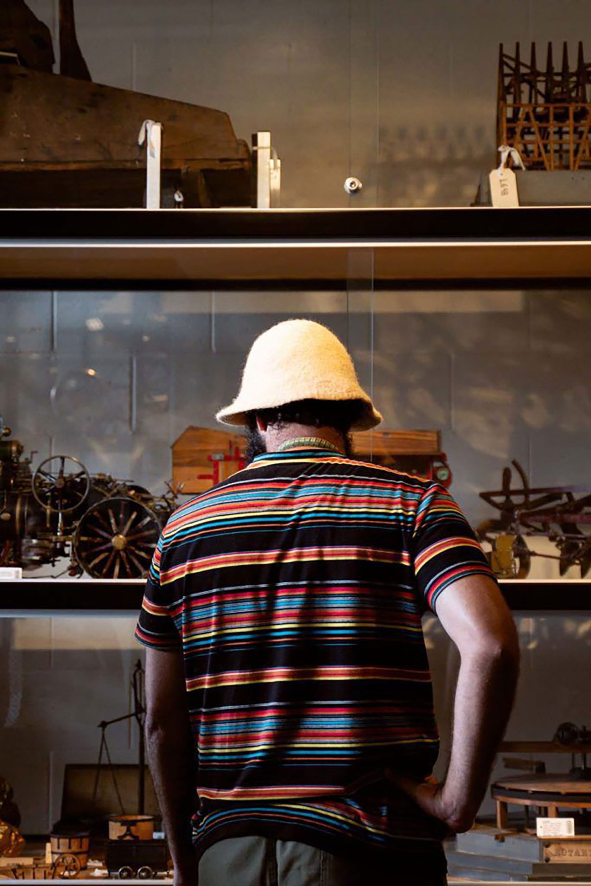 Joseph Douglas seen from behind standing in front of three shelves filled with various wooden objects.