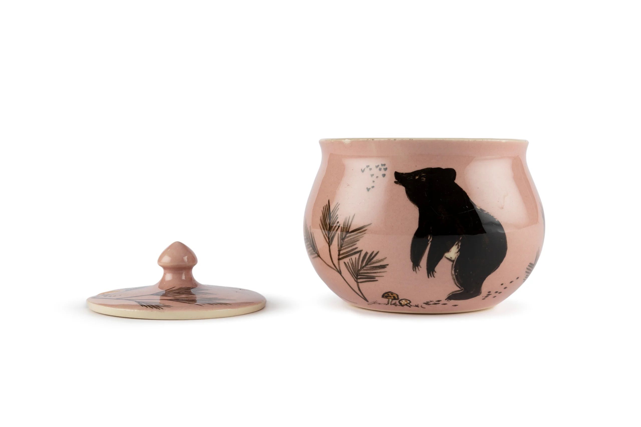 Object name: Honey jar made by Martin Boyd Pottery   Object No. 91/852   Link: here   Image: 13_martin boyd.jpeg   Alt text: A ceramic musk coloured open jar with an illustration of a bear looking at bees, a plant and mushrooms on the ground. The lid is to the left.