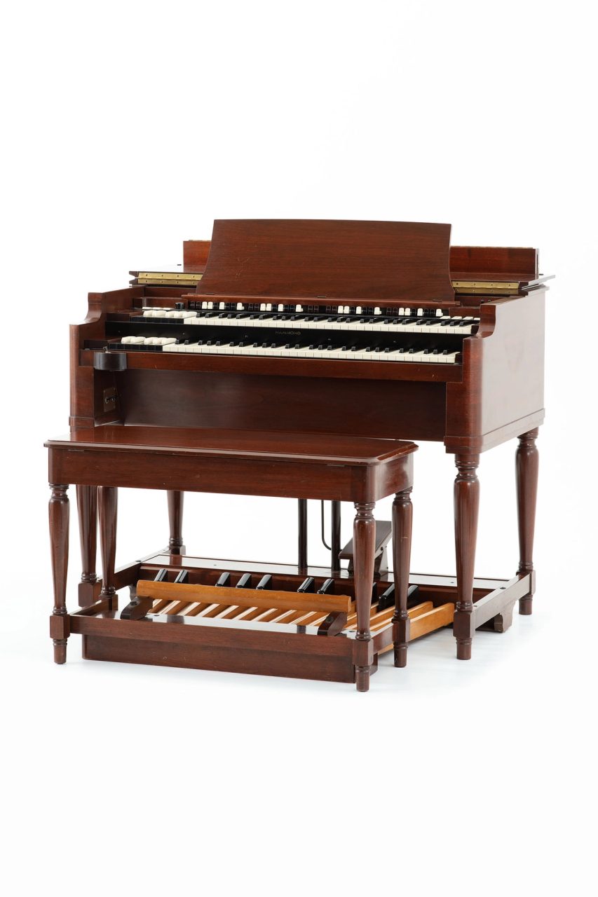 A wooden electric organ with matching stool. It has two keyboards and a range of foot pedals.