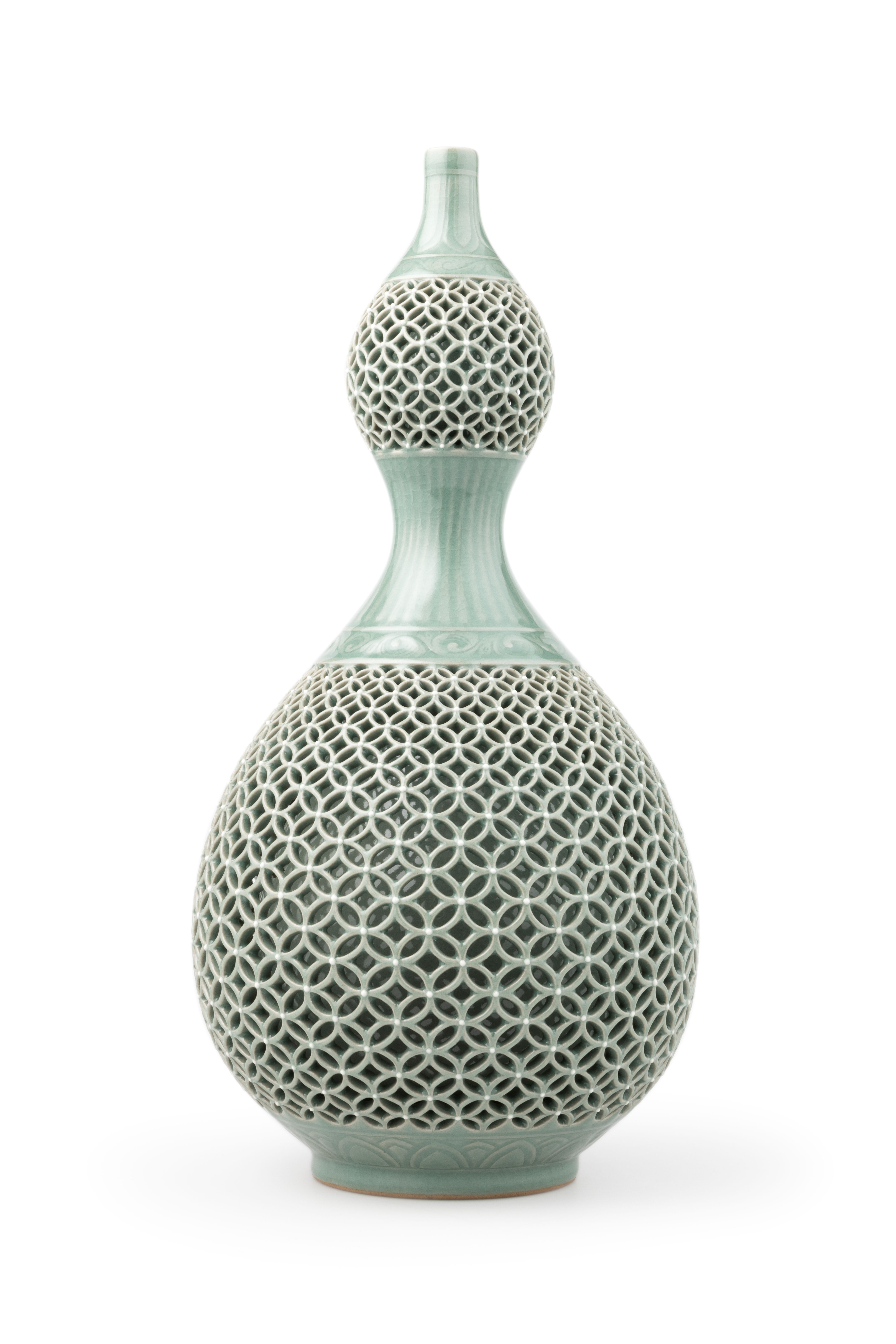 A double-layered jade green (celadon) bottle in a gourd shape. The outer ware features an openwork design of the seven treasures motif, where interlocking circles which graduate in size from the top of the pattern to the middle and then decrease towards the base. A leaf pattern is also featured on the top, middle and base of the celadon bottle outer ware. Maker's mark on base.