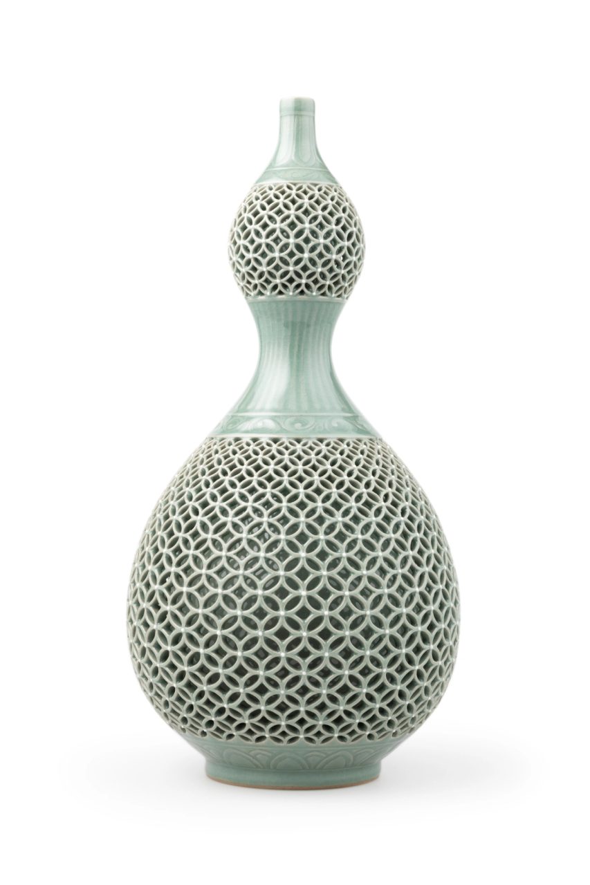 A double-layered jade green (celadon) bottle in a gourd shape. The outer ware features an openwork design of the seven treasures motif, where interlocking circles which graduate in size from the top of the pattern to the middle and then decrease towards the base. A leaf pattern is also featured on the top, middle and base of the celadon bottle outer ware. Maker's mark on base.