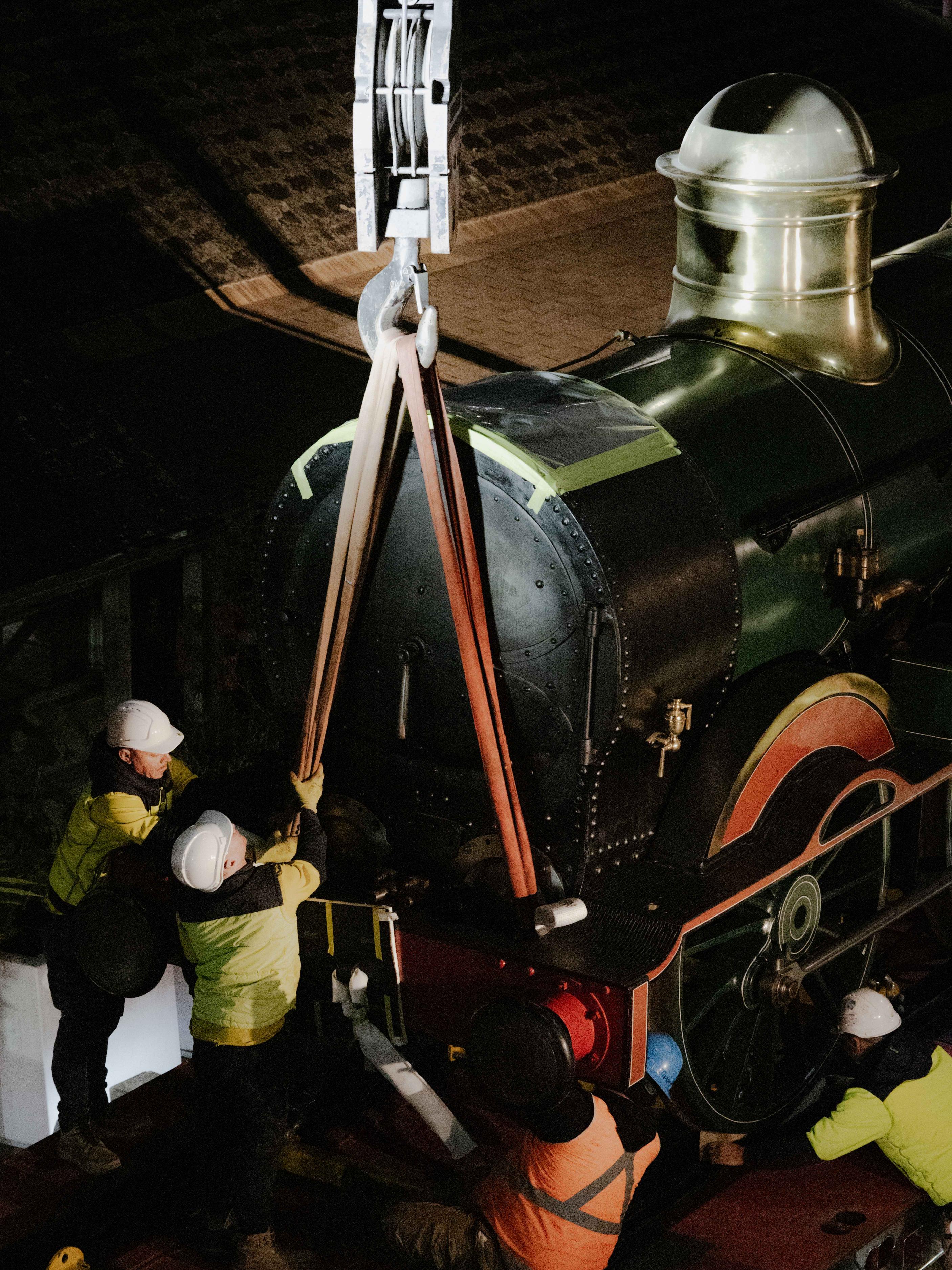 Trades people rigging up a train to a crane.