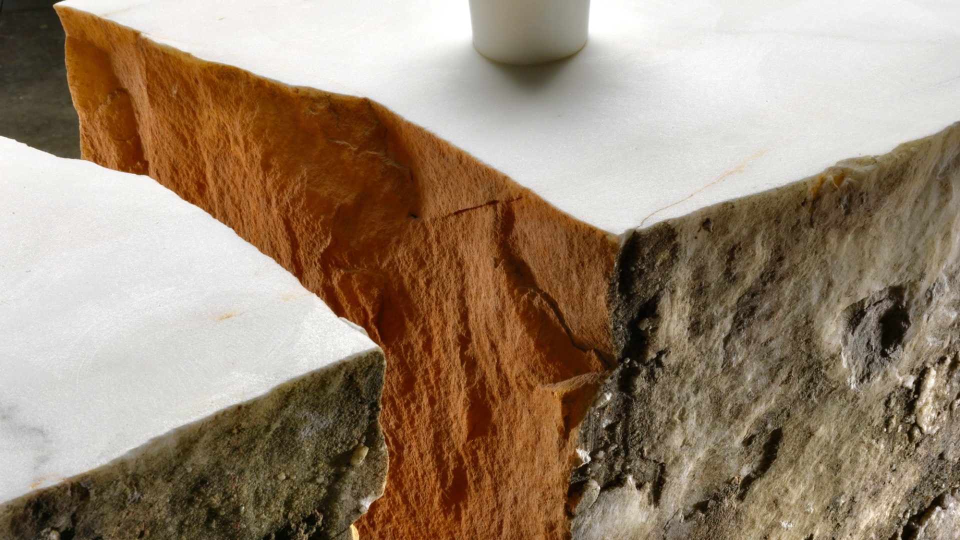 Detail image of a corner of an orange, white and beige coloured stone table with a protruding white cylindrical rod