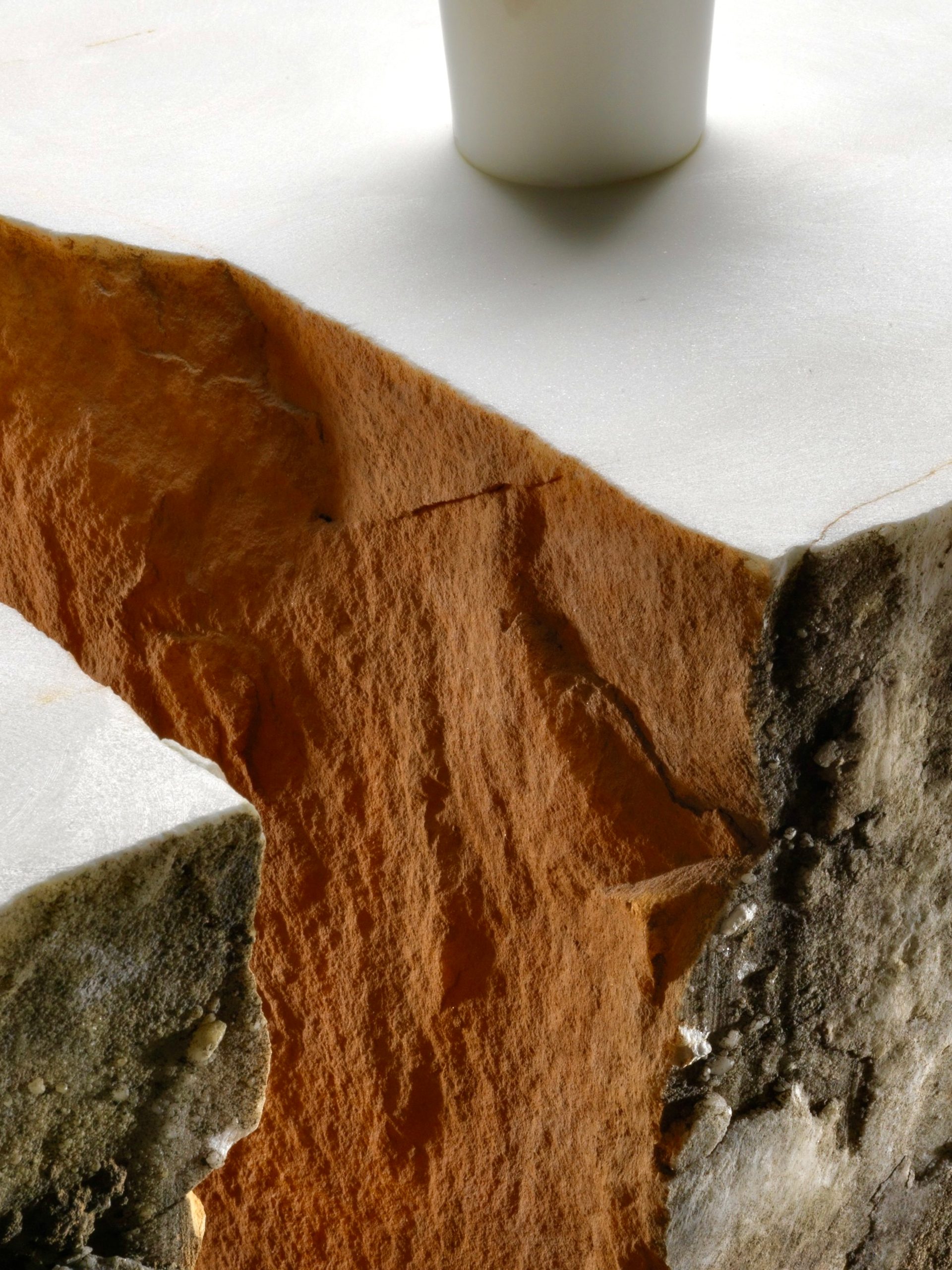 Detail image of a corner of an orange, white and beige coloured stone table with a protruding white cylindrical rod