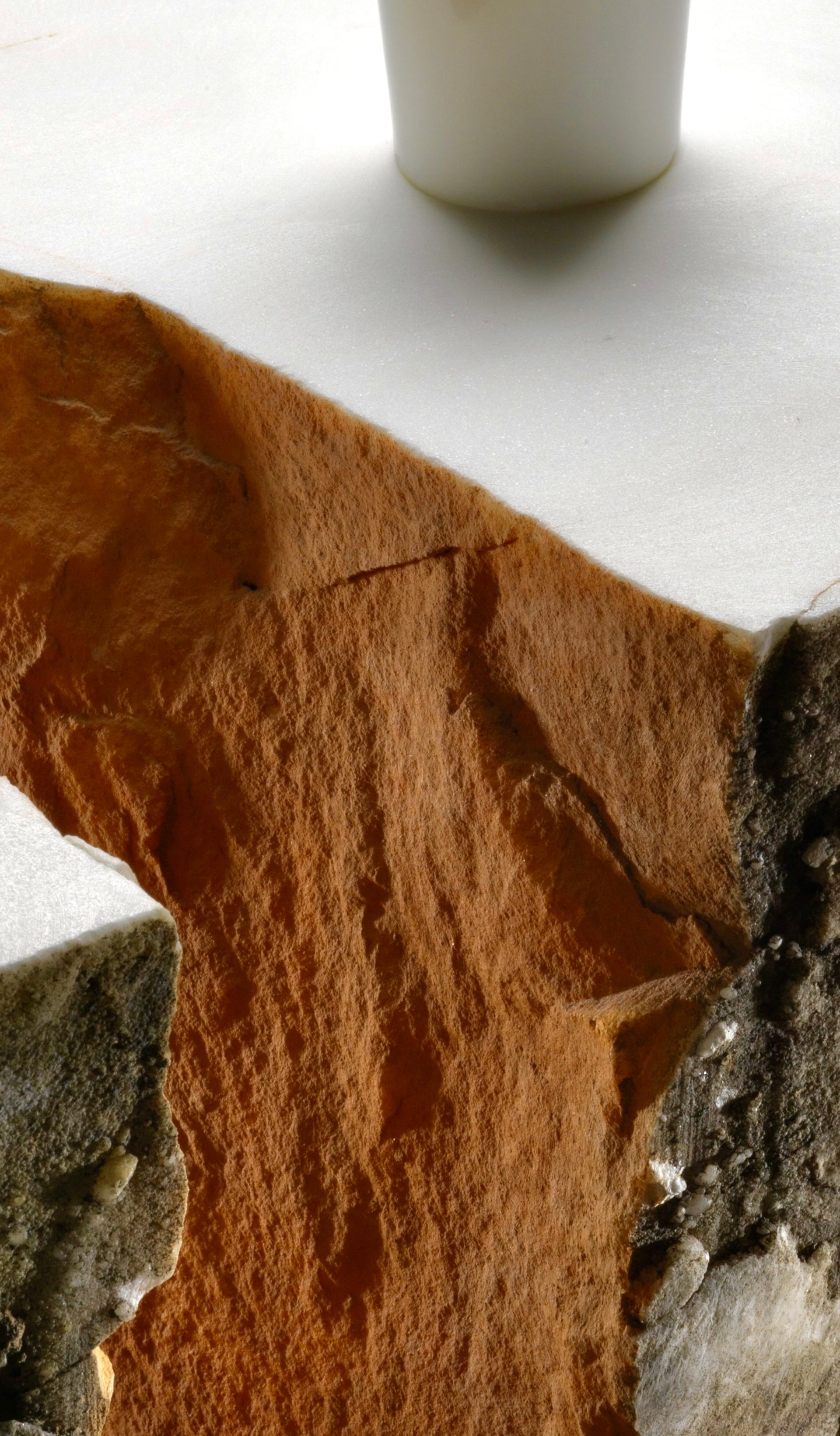Detail image of a corner of an orange, white and beige coloured stone table with a protruding white cylindrical rod