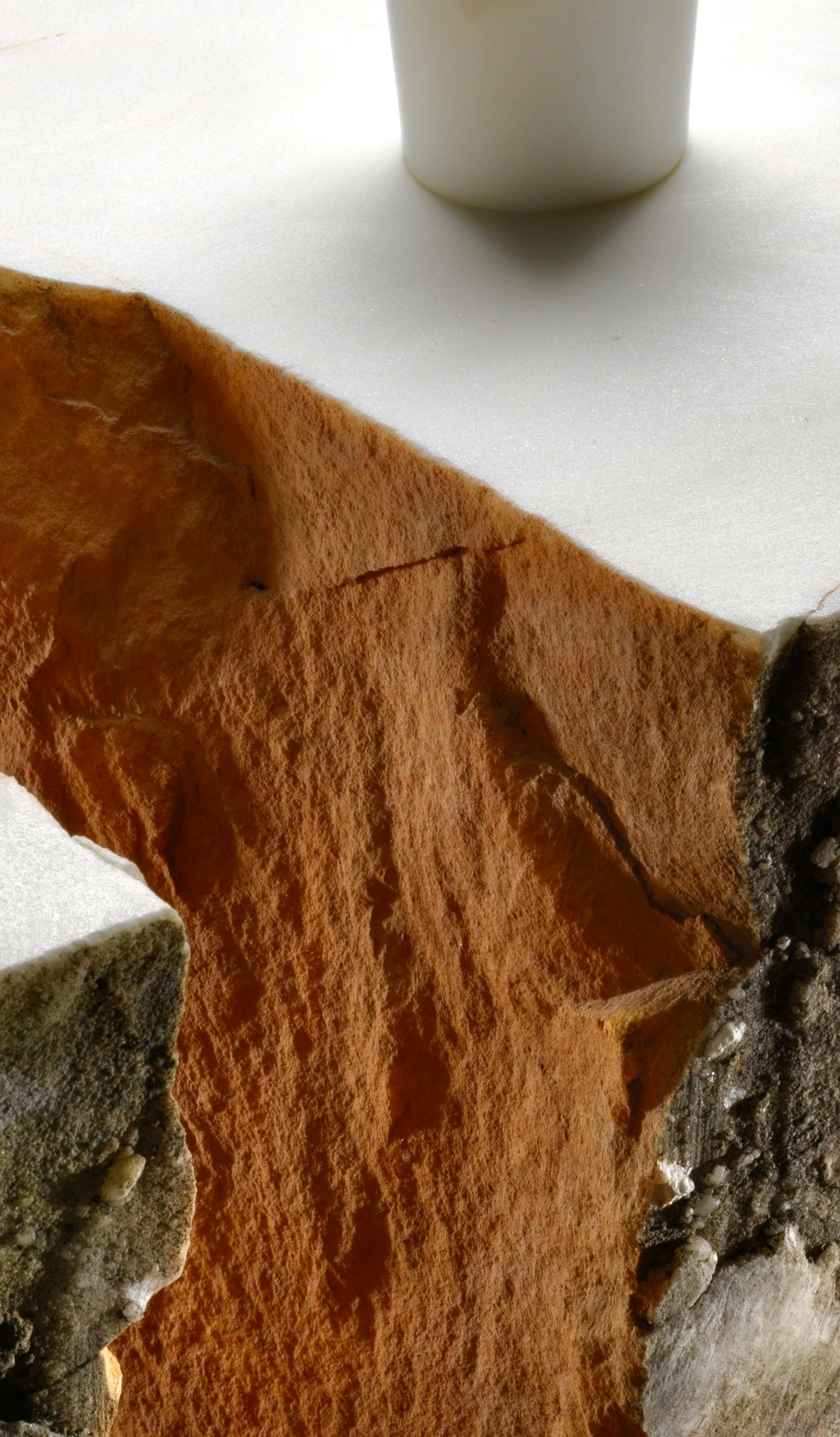 Detail image of a corner of an orange, white and beige coloured stone table with a protruding white cylindrical rod