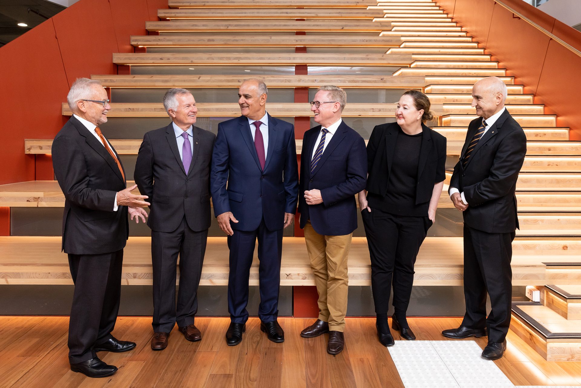 Six people stand and pose for a photo, they are smiling at each other.