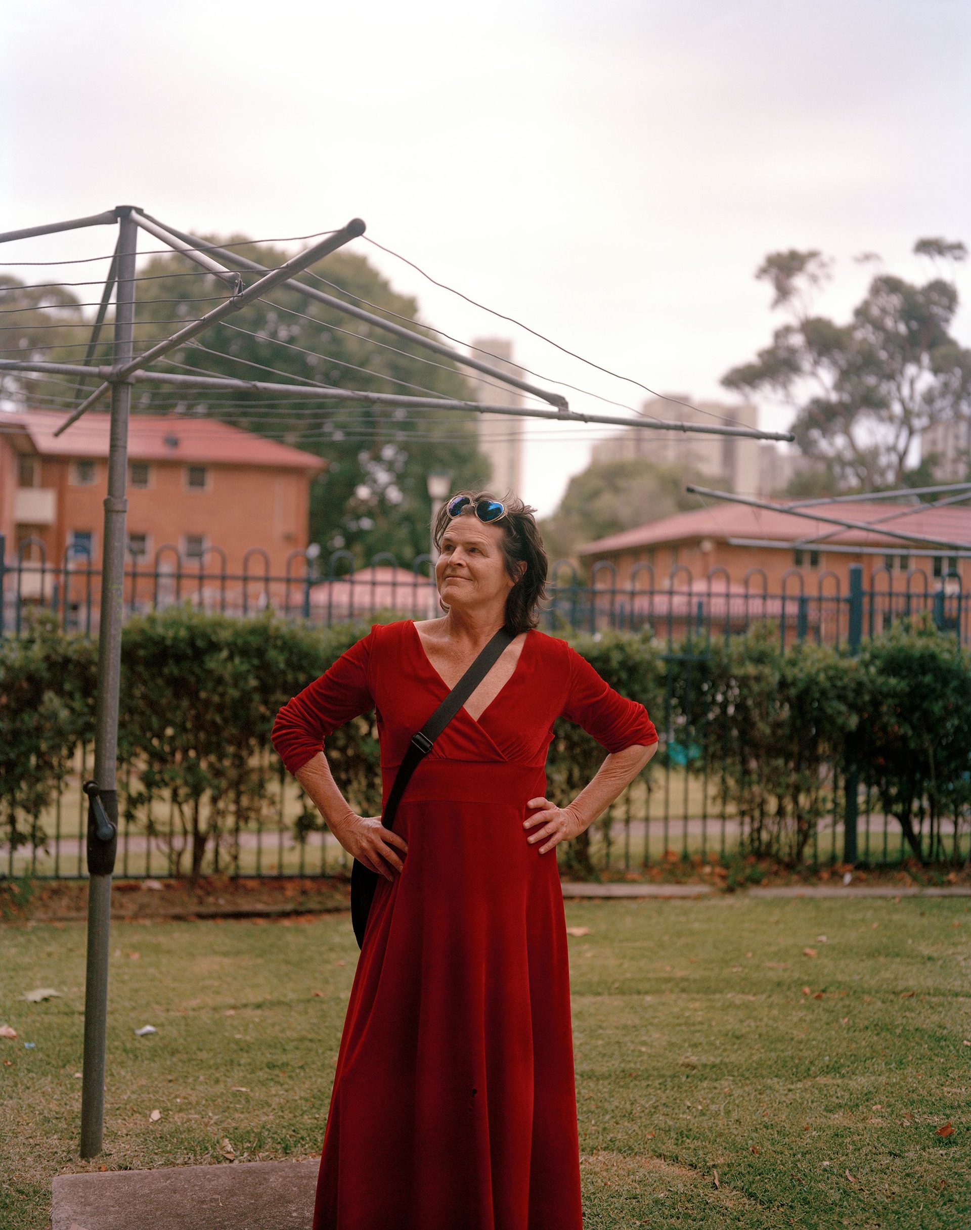 A person stands outside, in front of a Hills Hoist clothesline. They are wearing a red dress and have their hands on their hips.