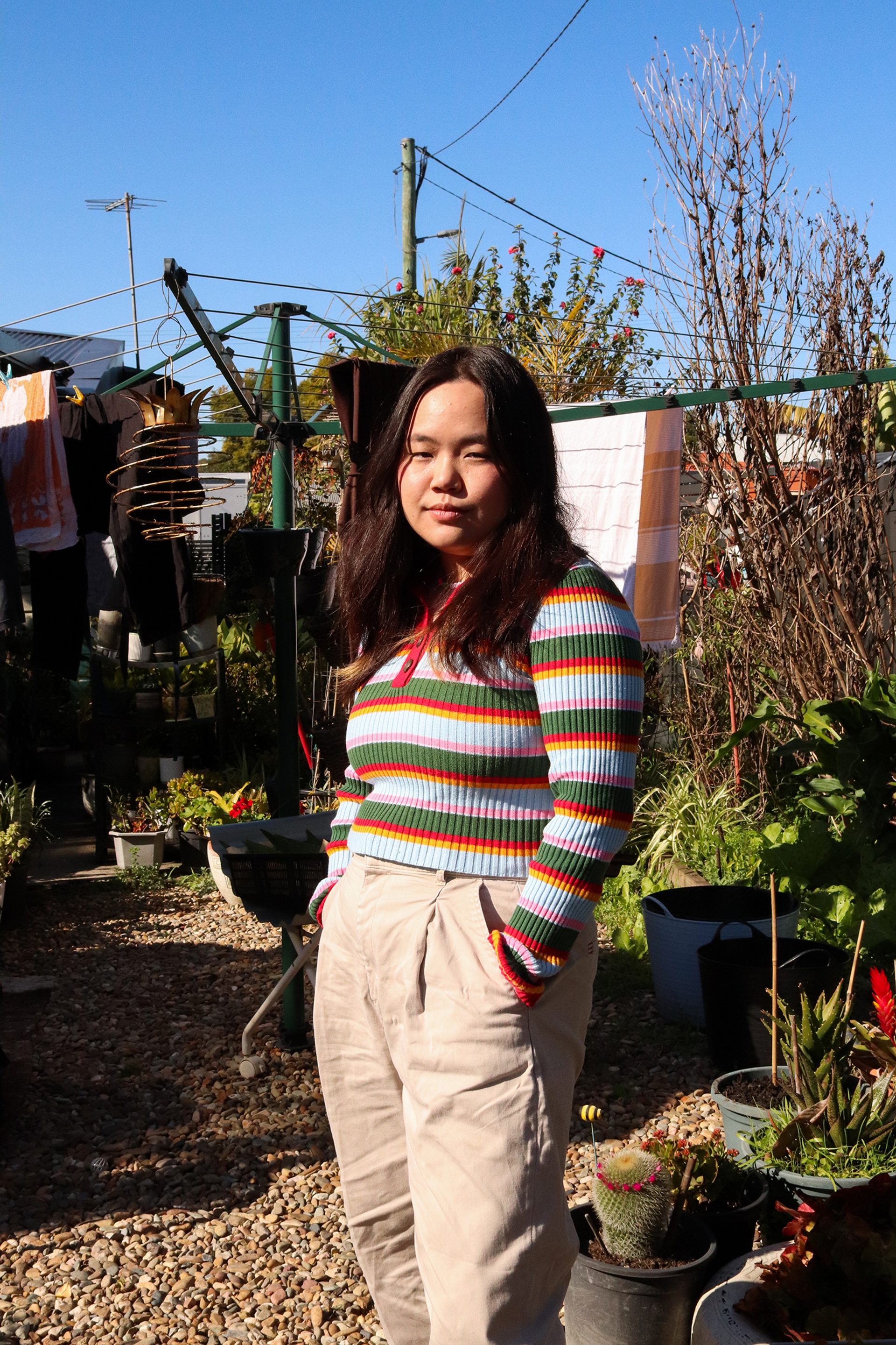 A young woman stands in a backyard. There is a hills hoist clothesline behind her with a few towels drying on it.