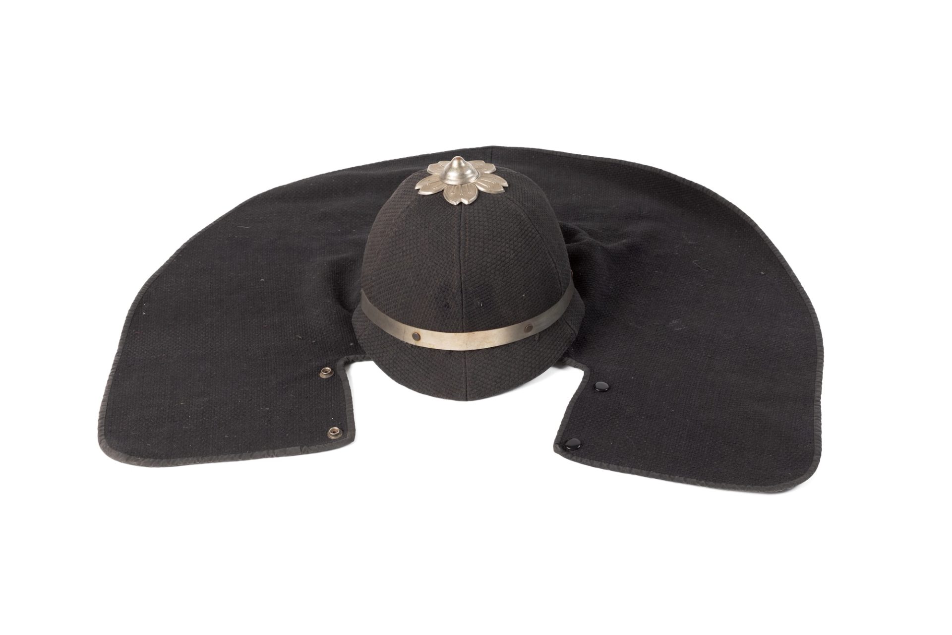 Photograph of a dark indigo helmet made of cotton, part of Japanese fireman's costume. Attached to the helmet is a long piece of fabric used to cover the firefighters head, including a flower/sakura shaped piece of metal on the top of the helmet.