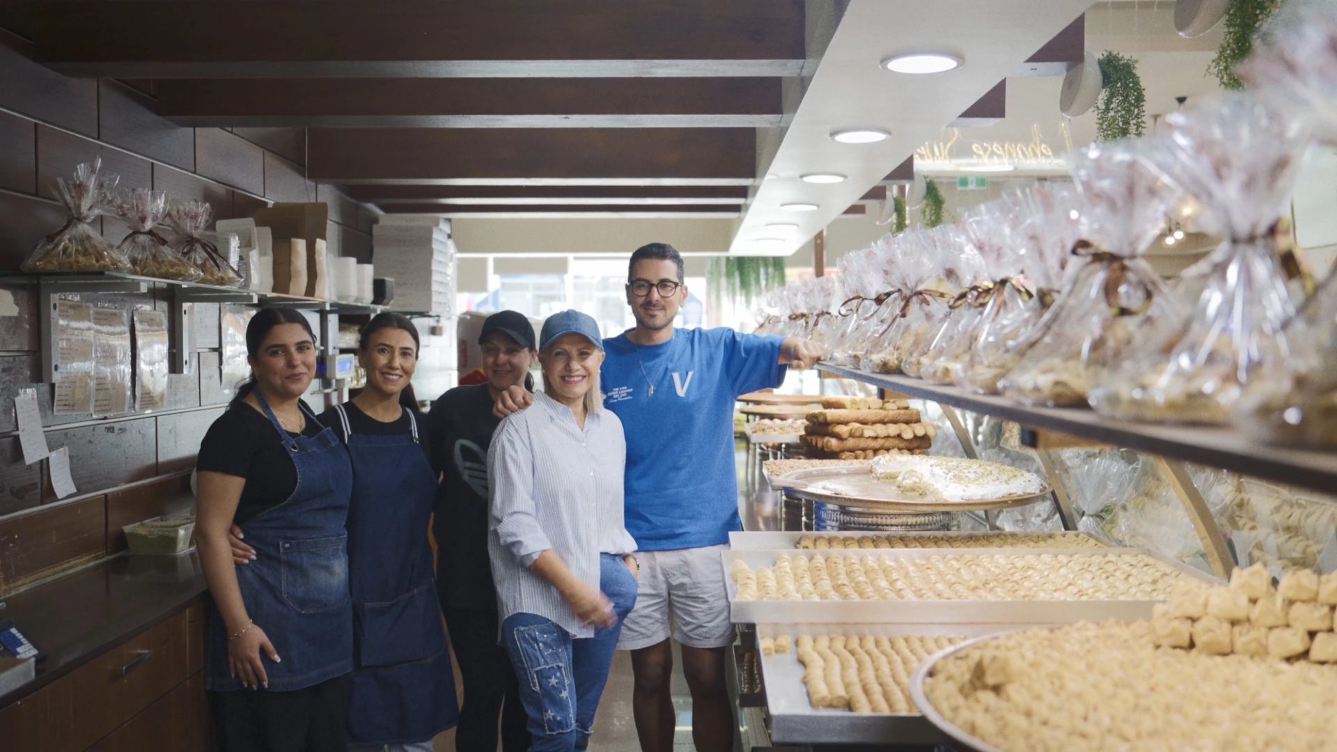 5 people standing and smiling behind a sweets display.