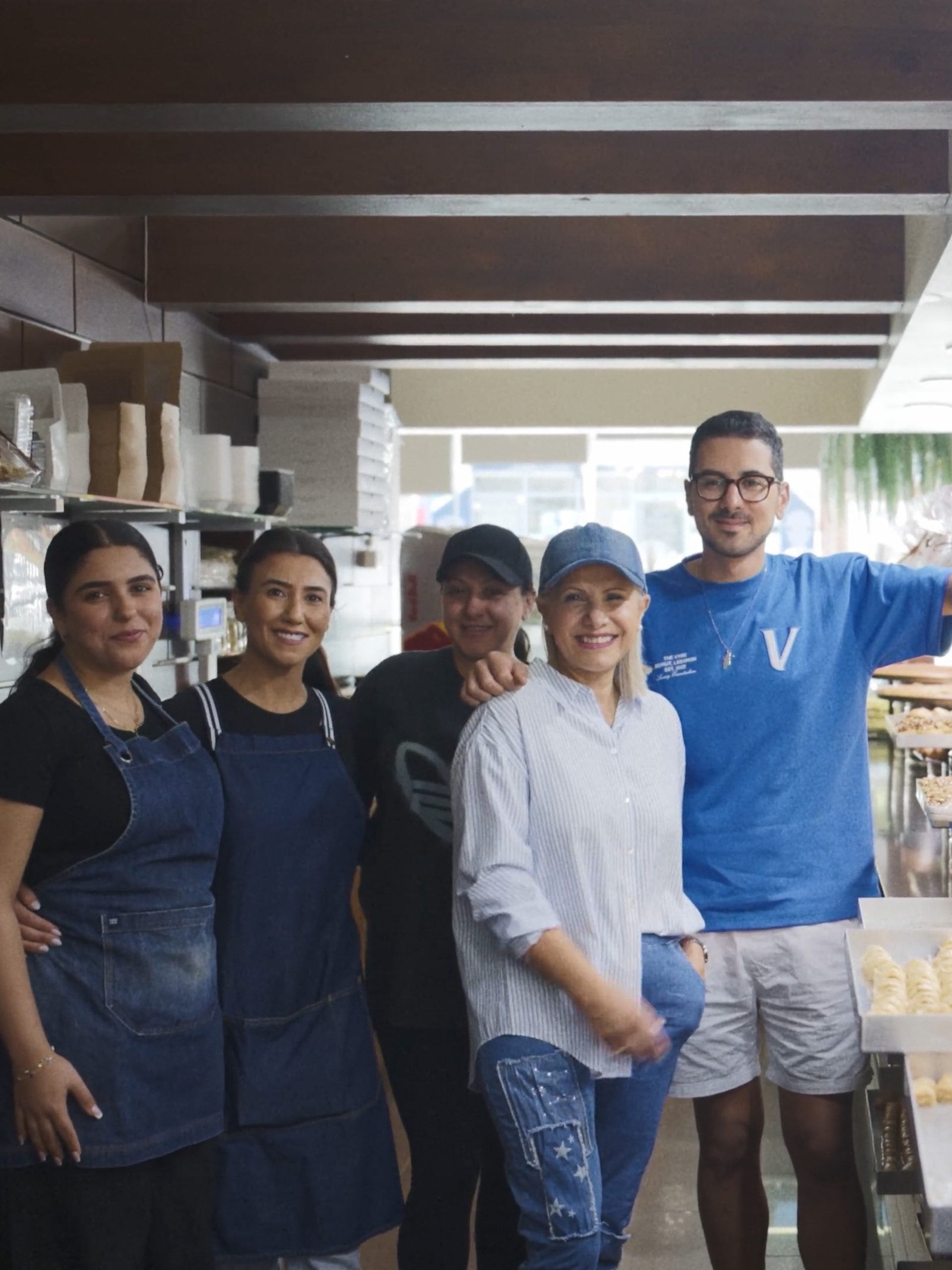 5 people standing and smiling behind a sweets display.