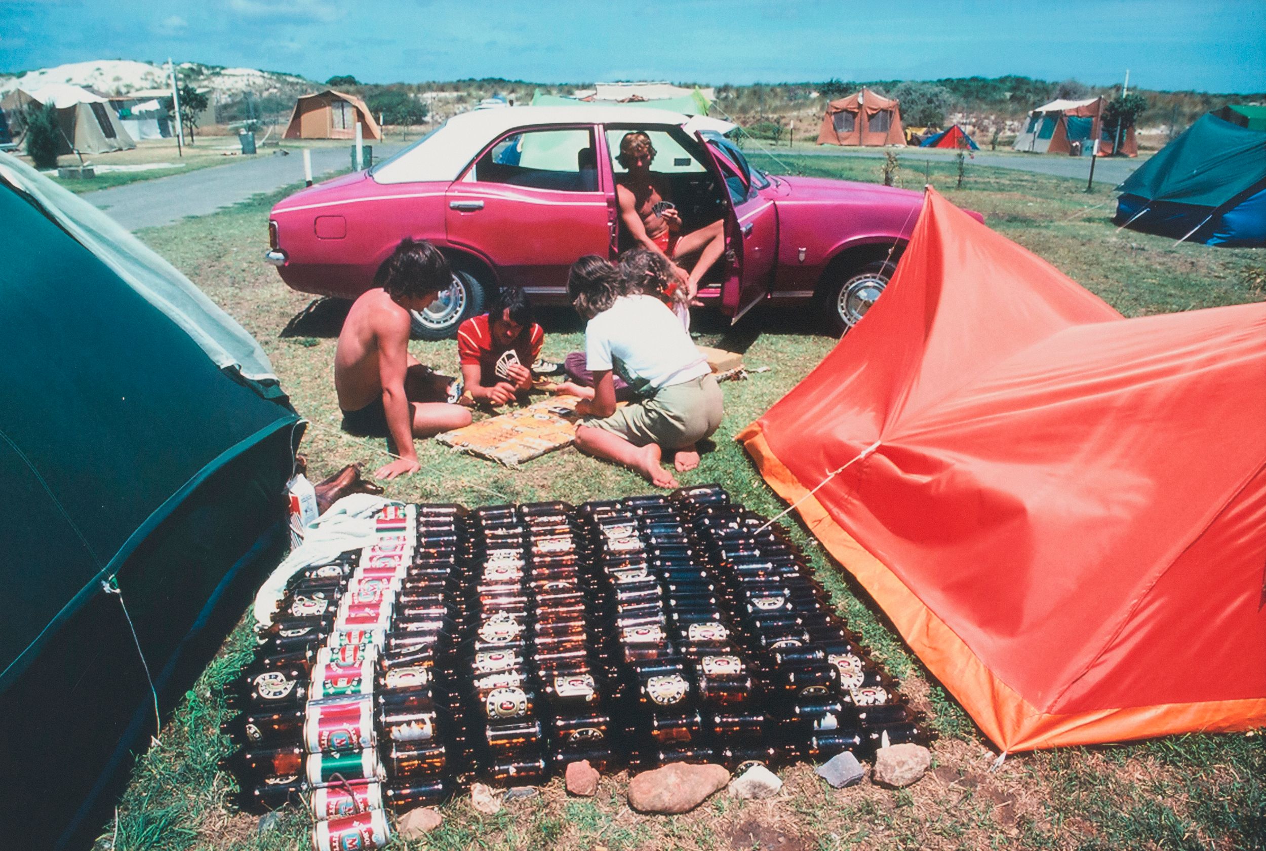 People camping next to a car with lots of beer stacked up inbetween