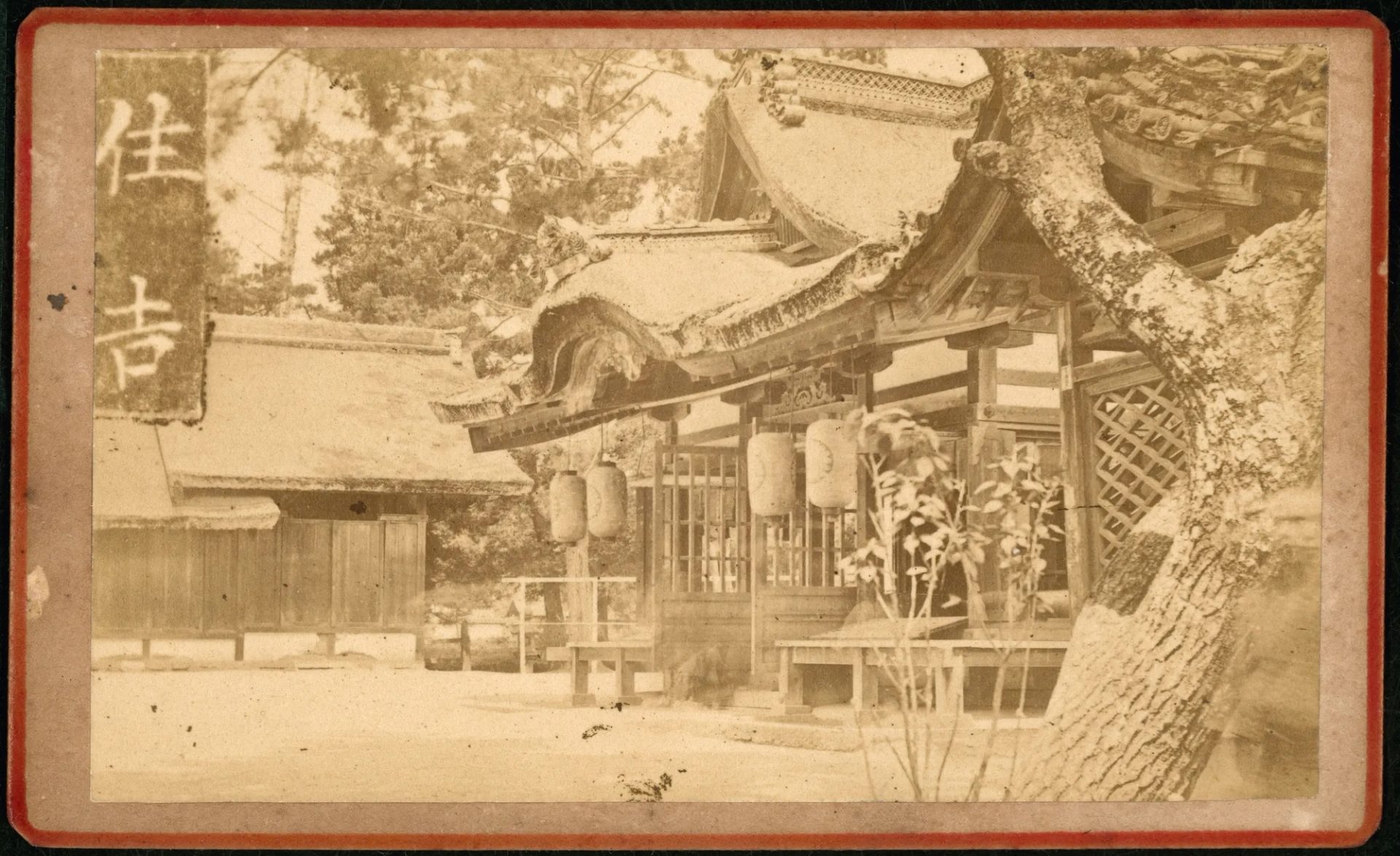 A sepia printed photograph of Nichiren Temple in Osaka, Japan from the 1880s. Four paper lanterns at the entrance of a straw roof with intricate sculpture rims.